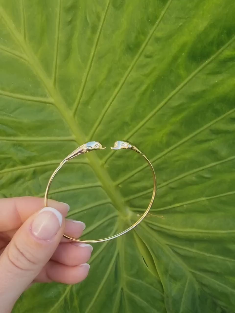 A 14k solid gold bangle bracelet for women, featuring a double dolphin head design.