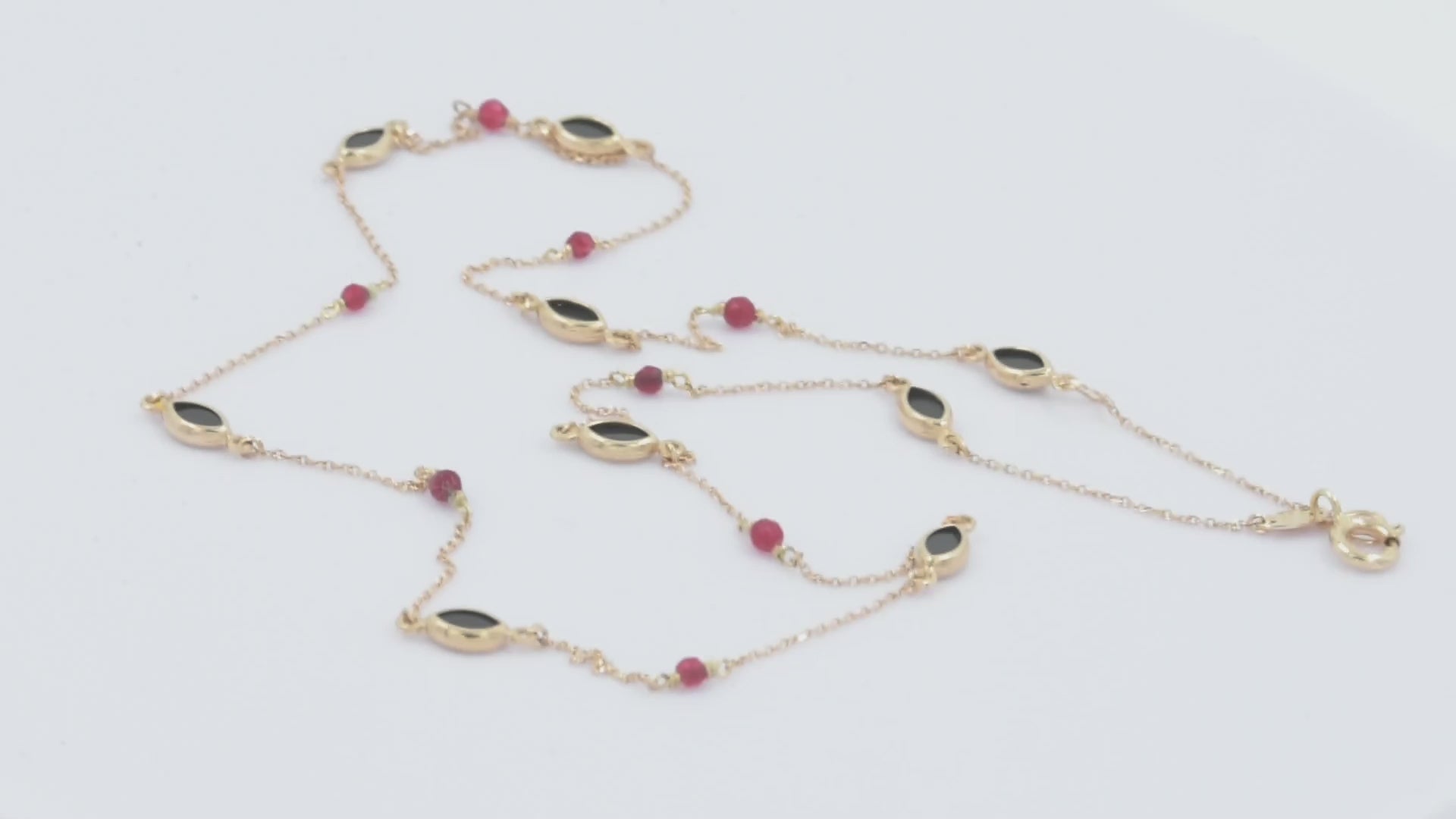 The photo shows a delicate gold necklace featuring small tourmaline gemstones and black marquise-shaped onyx accents, spaced along a fine chain. The contrasting colors create a striking and elegant design