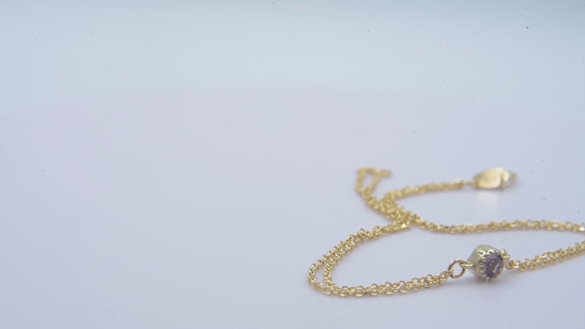 A handmade bracelet featuring a single birthstone set in 14k gold, complemented by a double chain design.