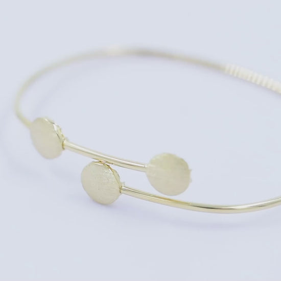 This photo features a minimalist gold open cuff bracelet with three textured round accents on the top.