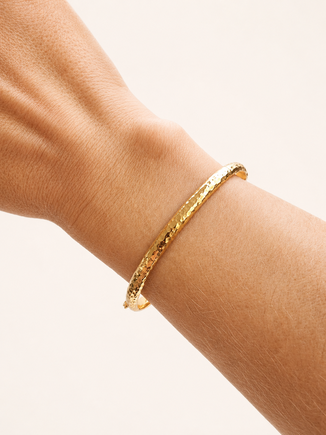 14k Gold hammered bangle bracelet on a wrist against a white background
