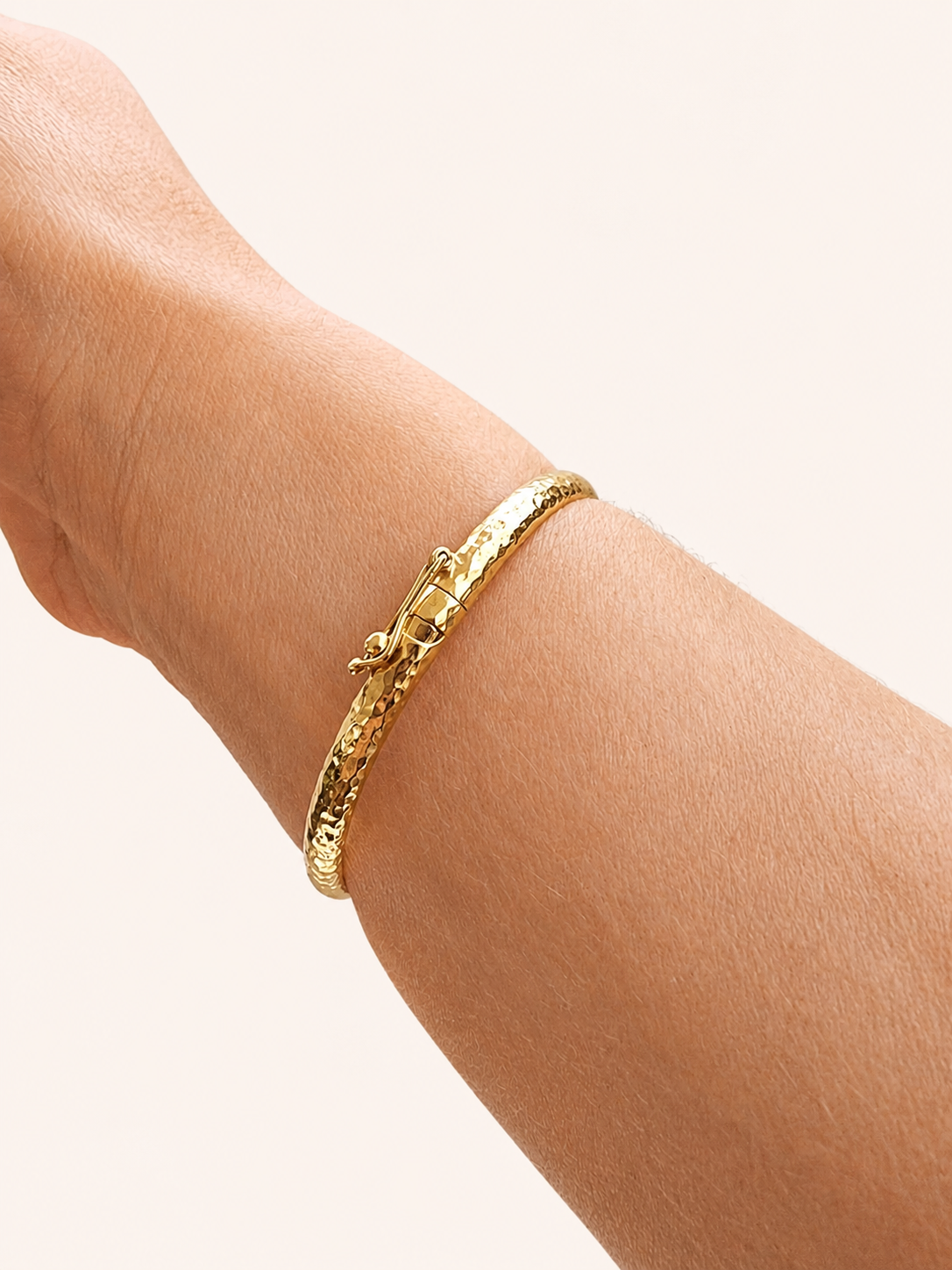 14k Gold hammered bangle bracelet on a wrist against a white background