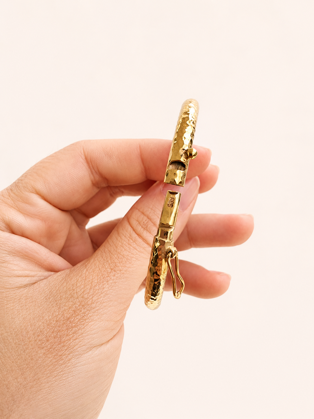14k Gold bangle bracelet held in a hand against a light background