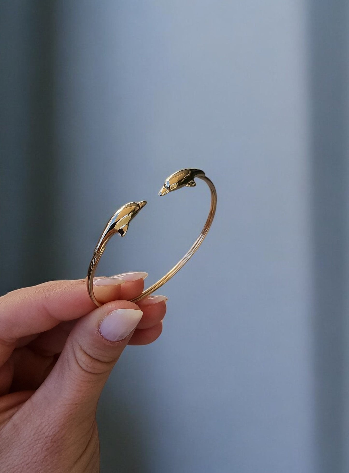 A 14k solid gold bangle bracelet for women, featuring a double dolphin head design.