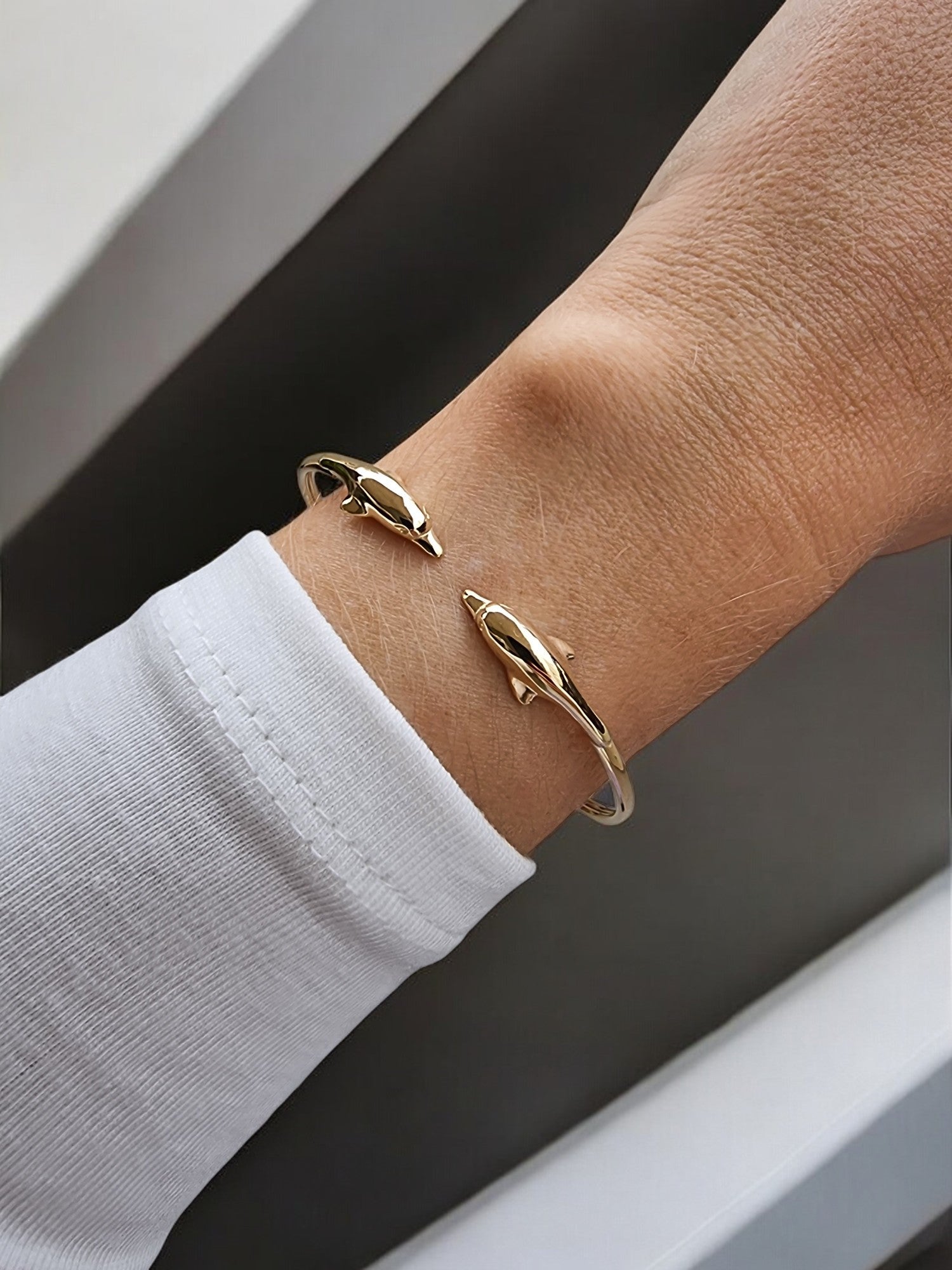 A 14k solid gold bangle bracelet for women, featuring a double dolphin head design.