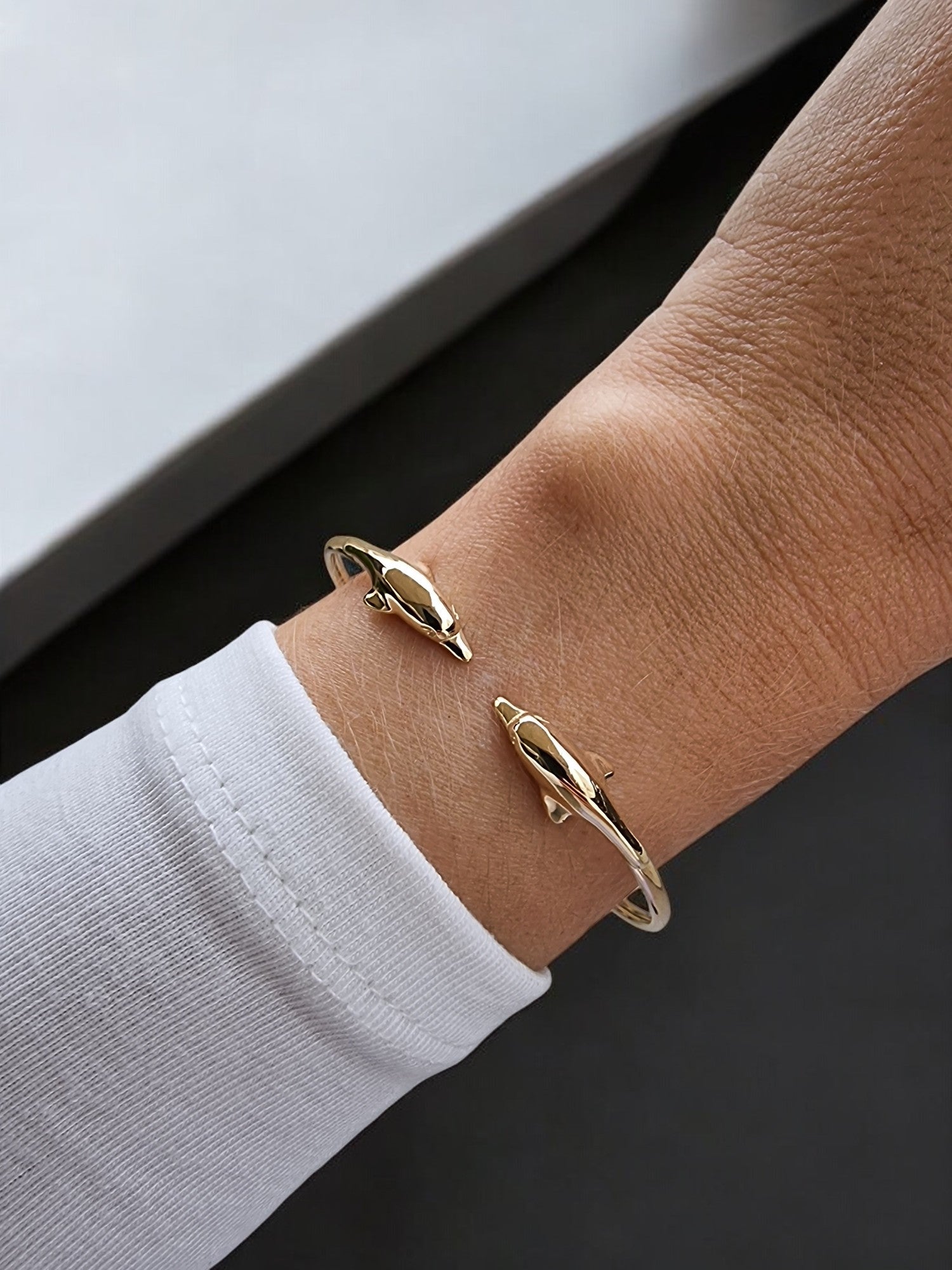 A 14k solid gold bangle bracelet for women, featuring a double dolphin head design.