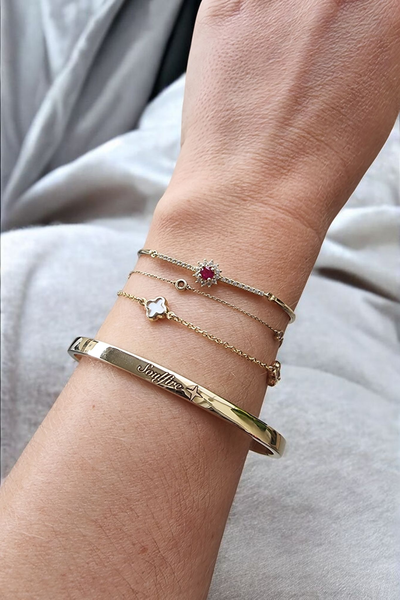 Close-up of a wrist wearing multiple gold bracelets with gemstones on a light gray background