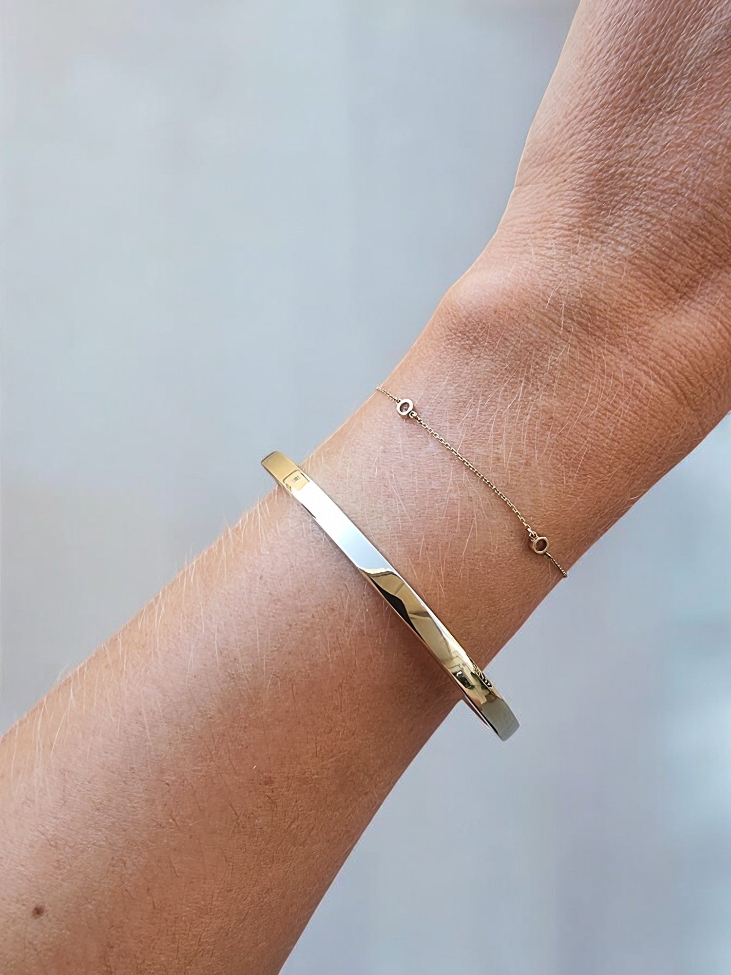 A 4.40mm open cuff bangle bracelet in 14k gold for women, paired with a delicate chain bracelet worn on a wrist.