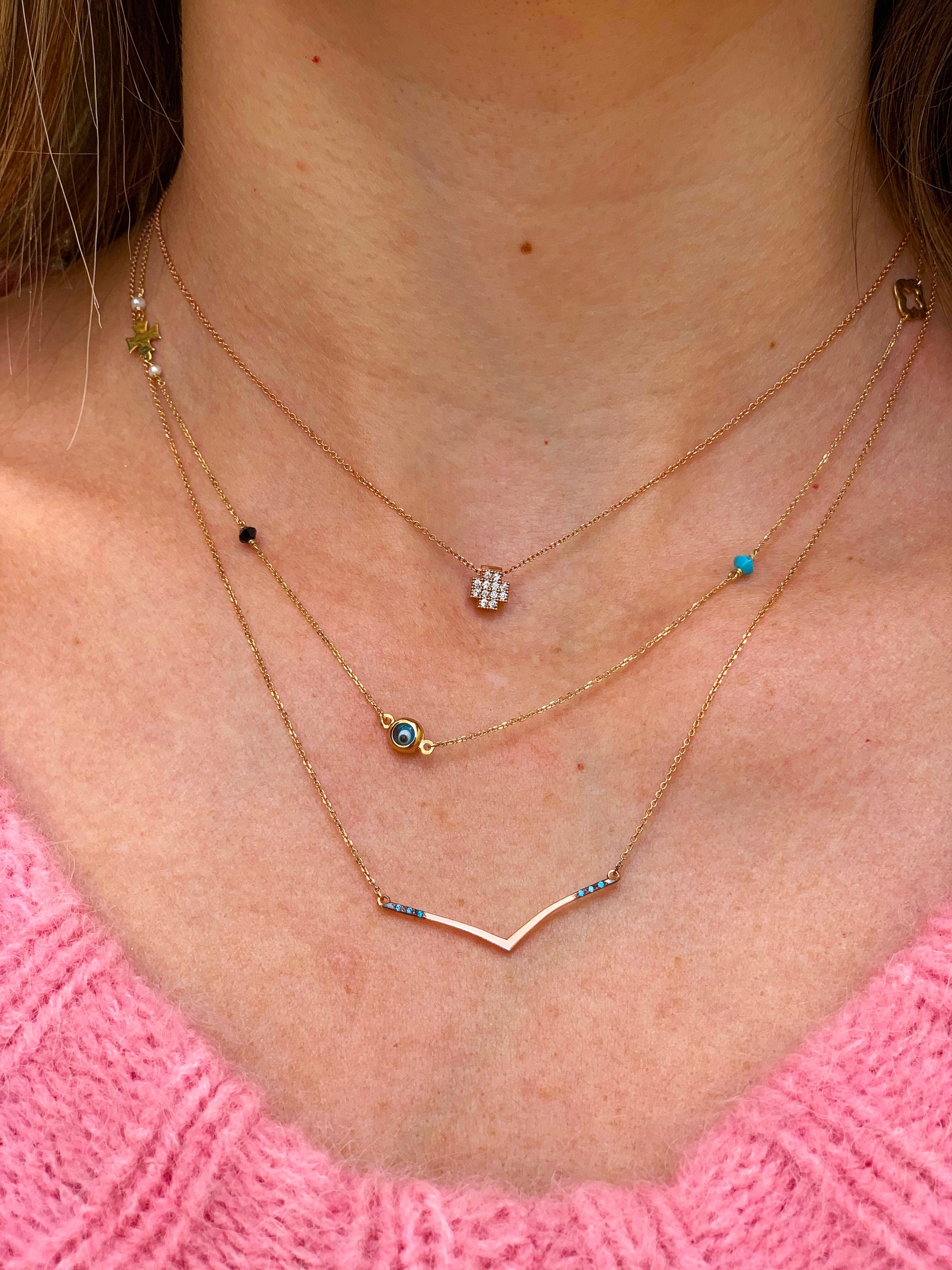 3 gold necklaces worn by a model, one cross, one shevron and one with multiple charms 