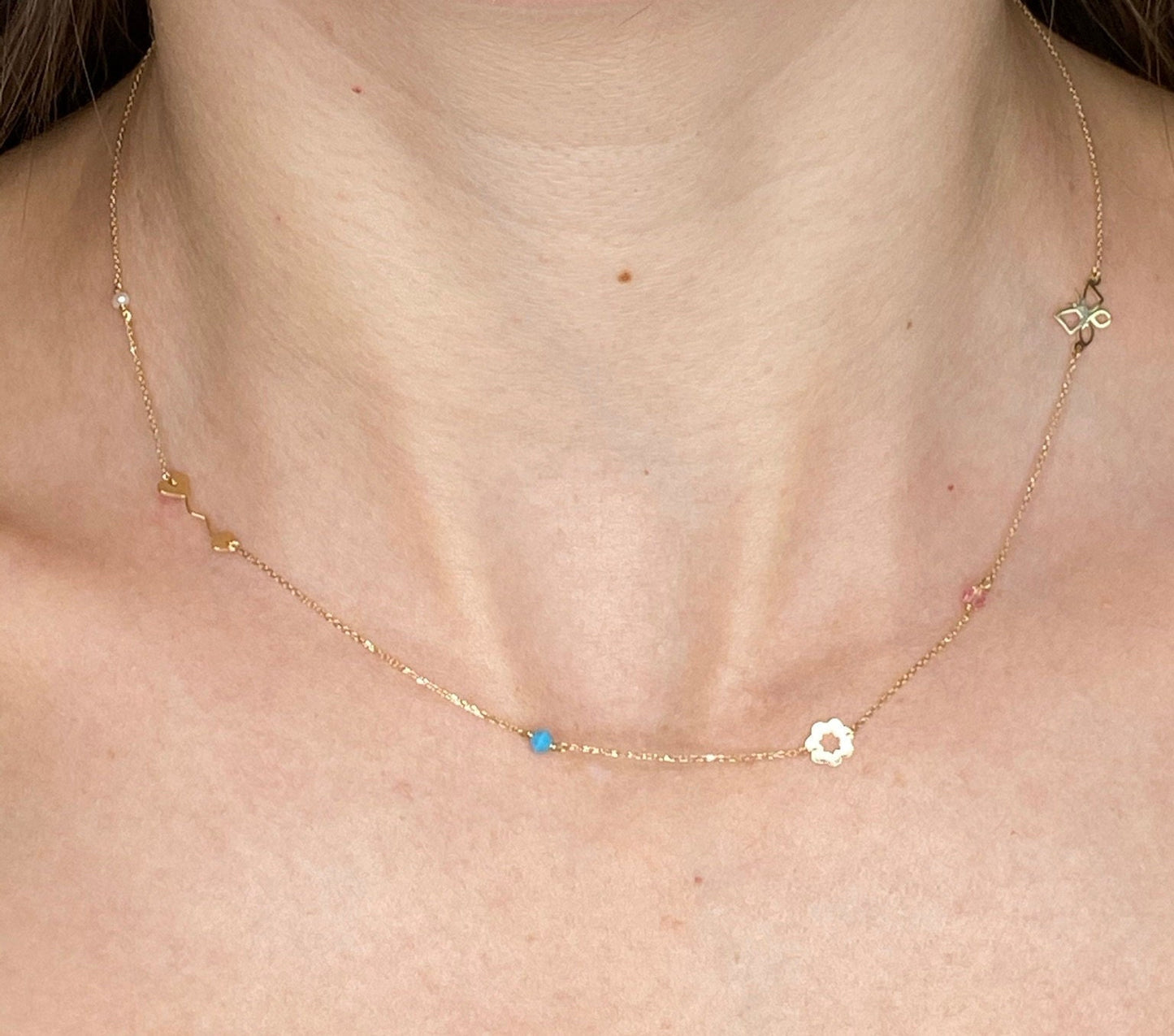 A station necklace featuring an arrow, flower, butterfly, pearl, turquoise, and a pink cubic zirconia stone.