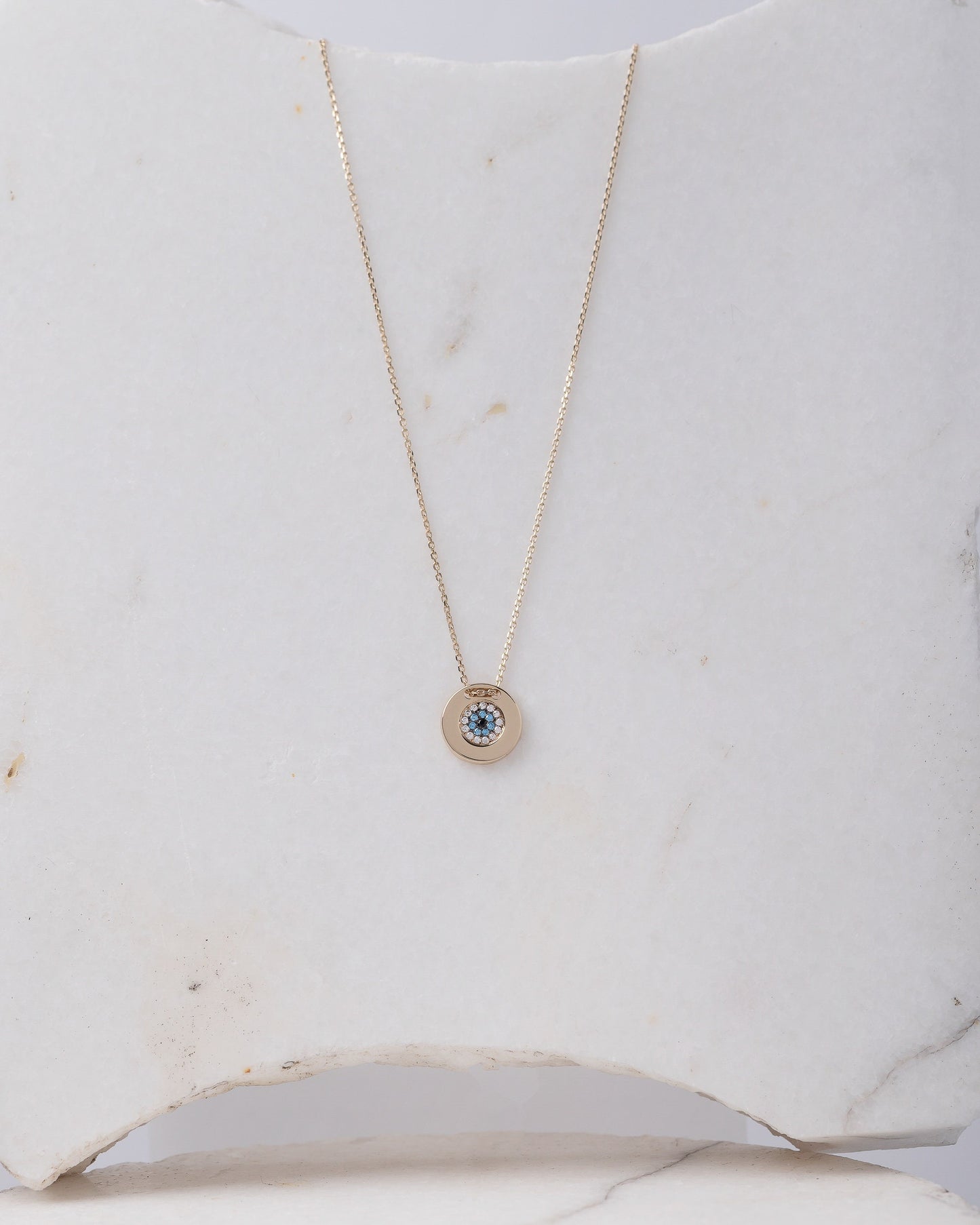 A women's round evil eye necklace, encrusted with cubic zirconia stones and crafted in 14k gold.