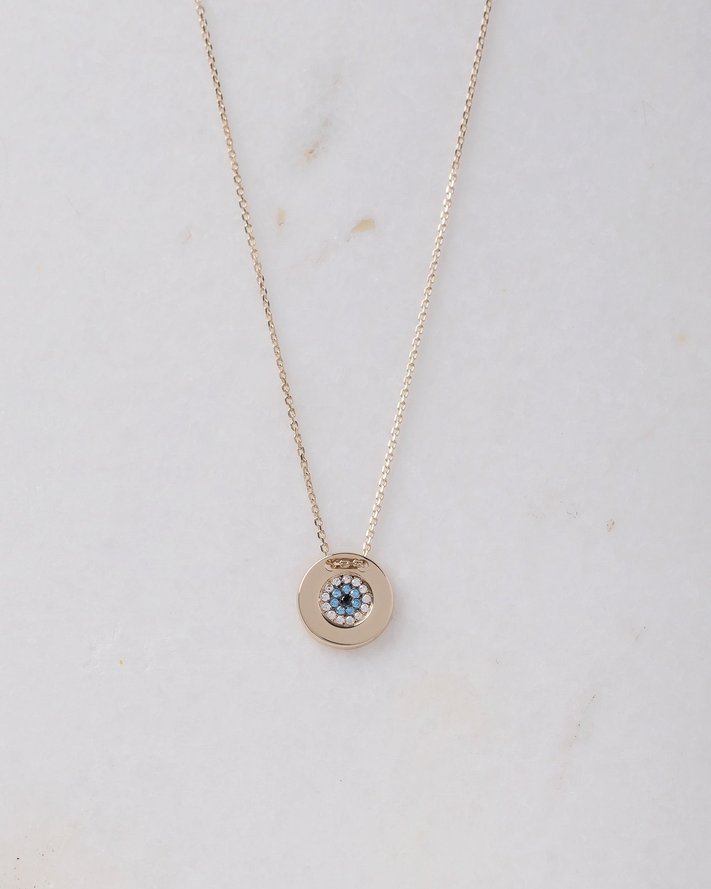 A women's round evil eye necklace, encrusted with cubic zirconia stones and crafted in 14k gold.