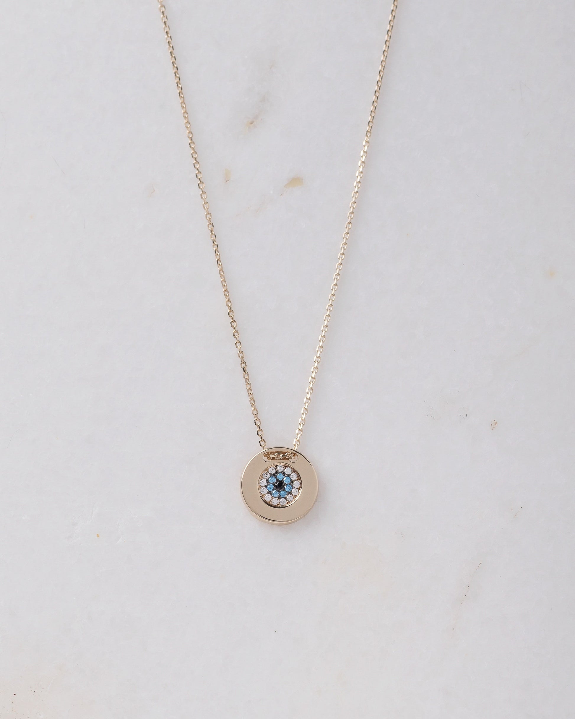 A women's round evil eye necklace, encrusted with cubic zirconia stones and crafted in 14k gold.