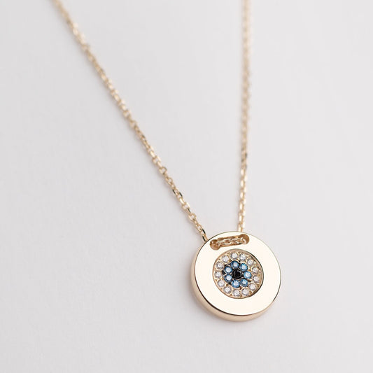 A women's round evil eye necklace, encrusted with cubic zirconia stones and crafted in 14k gold.