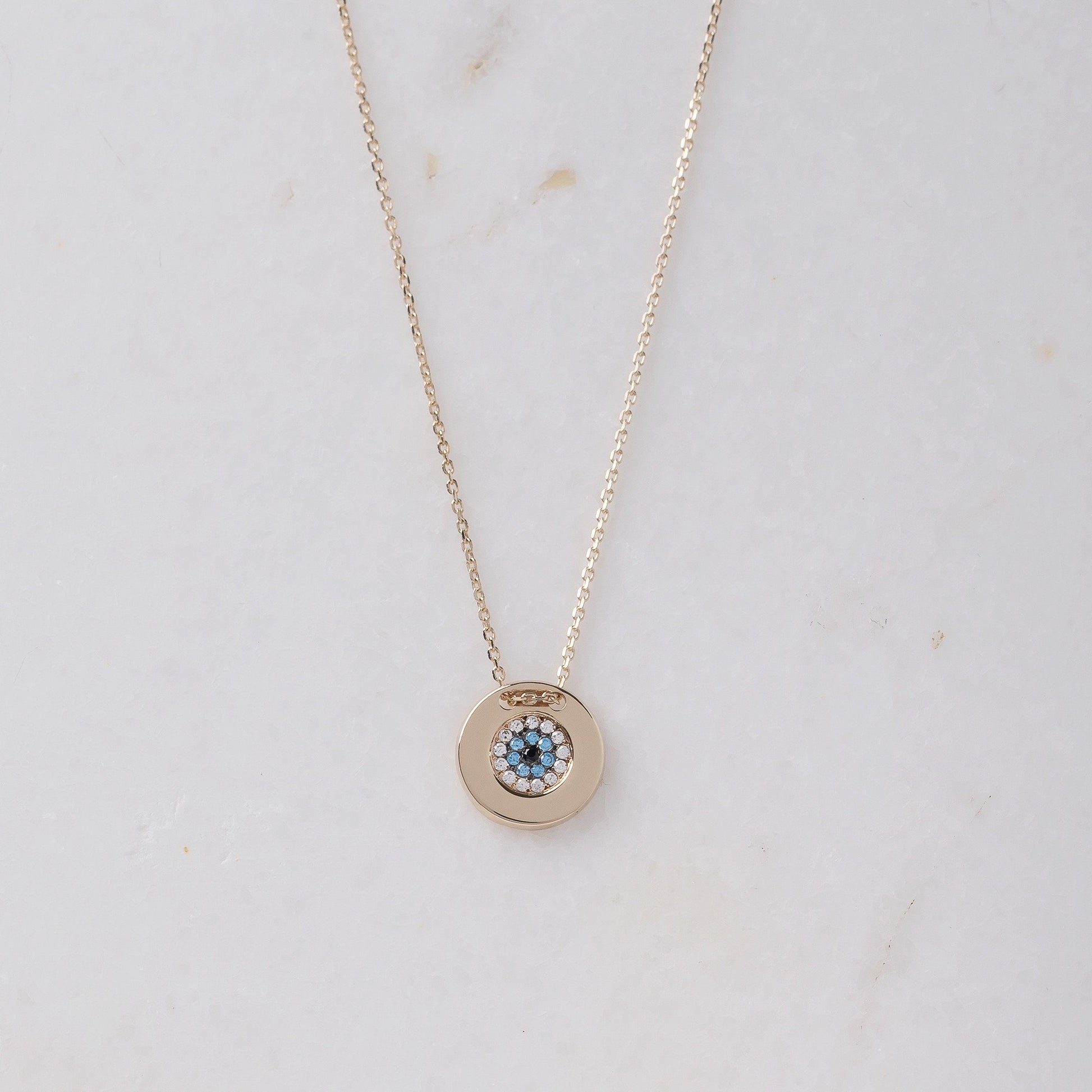 A women's round evil eye necklace, encrusted with cubic zirconia stones and crafted in 14k gold.