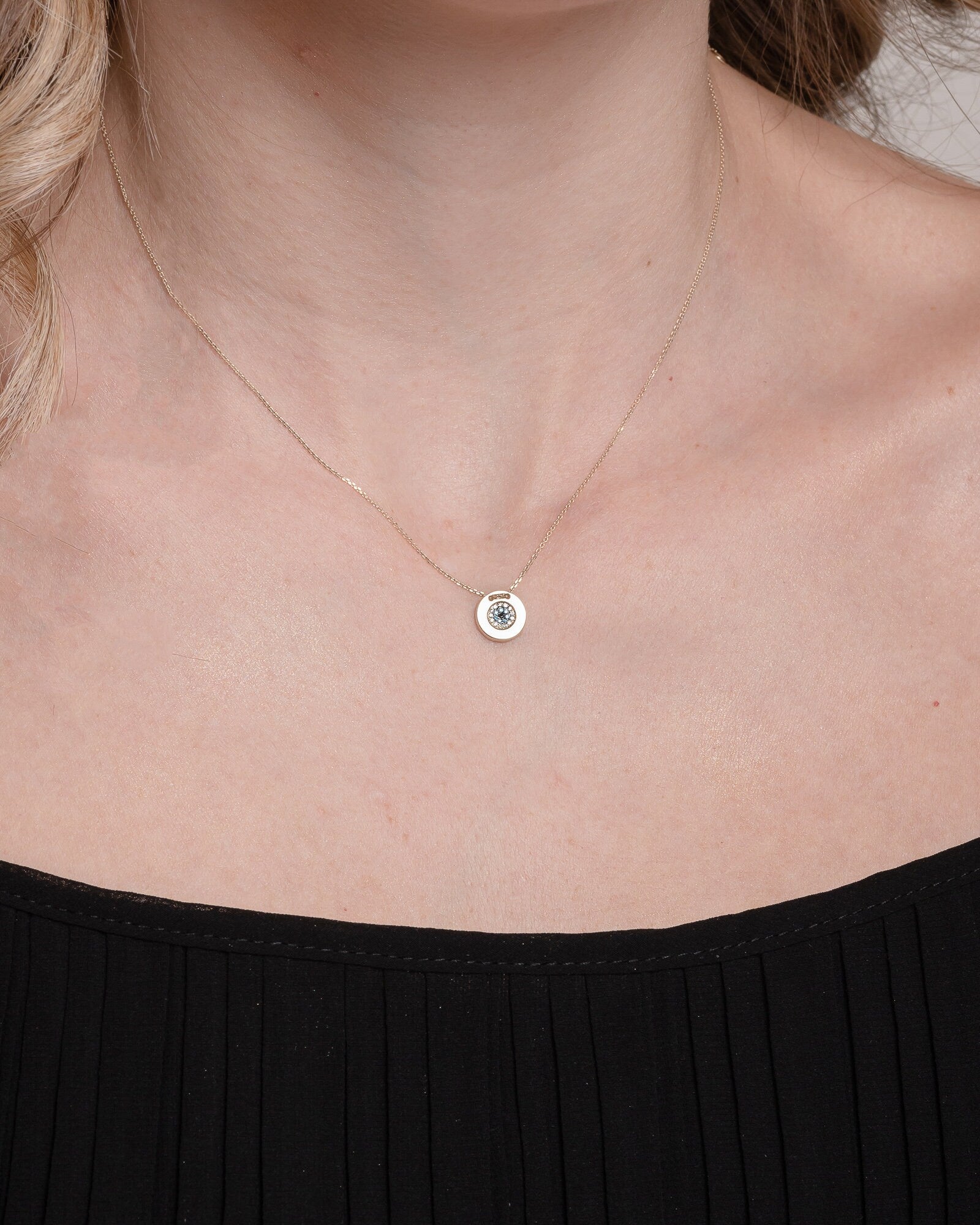 A women's round evil eye necklace, encrusted with cubic zirconia stones and crafted in 14k gold.