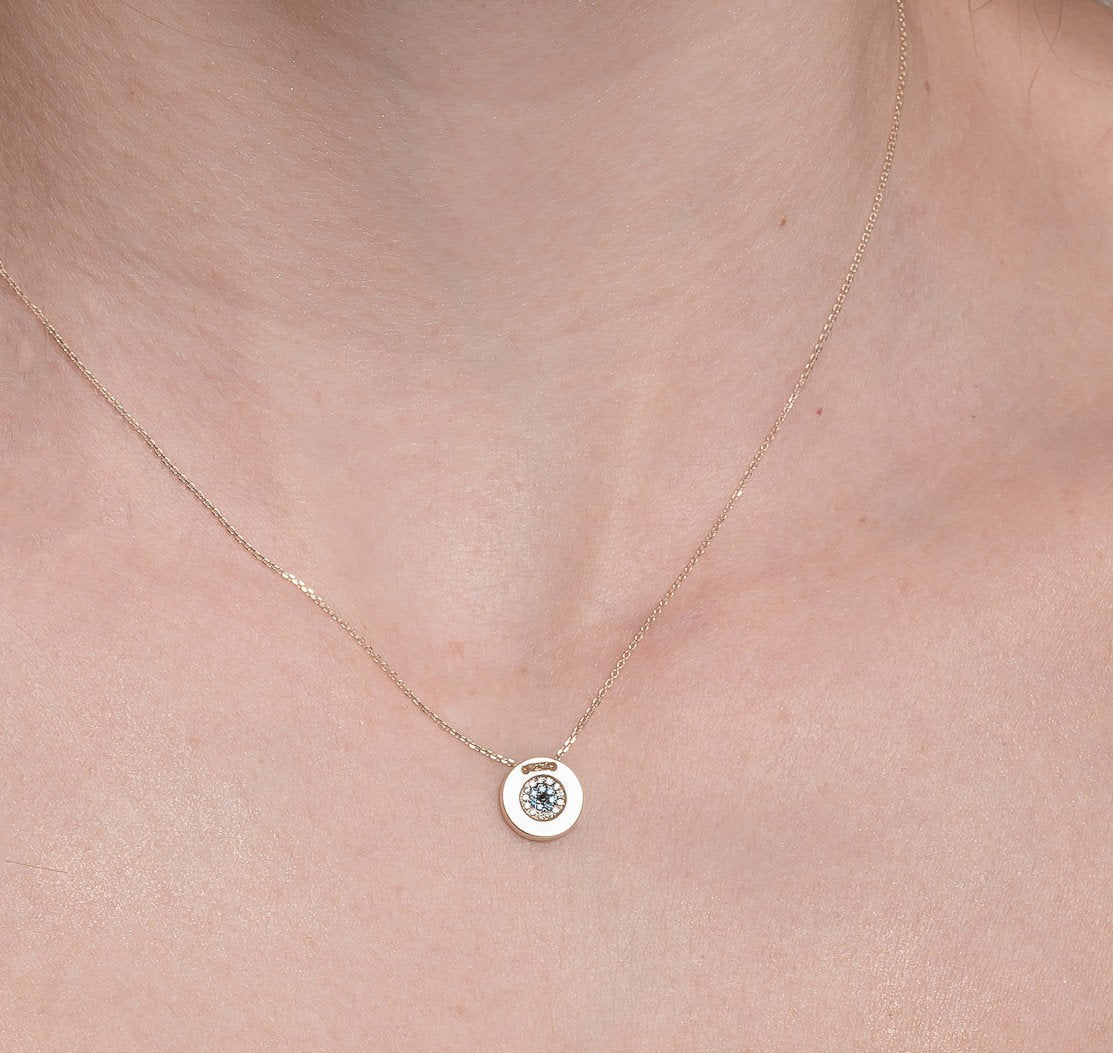 A women's round evil eye necklace, encrusted with cubic zirconia stones and crafted in 14k gold.