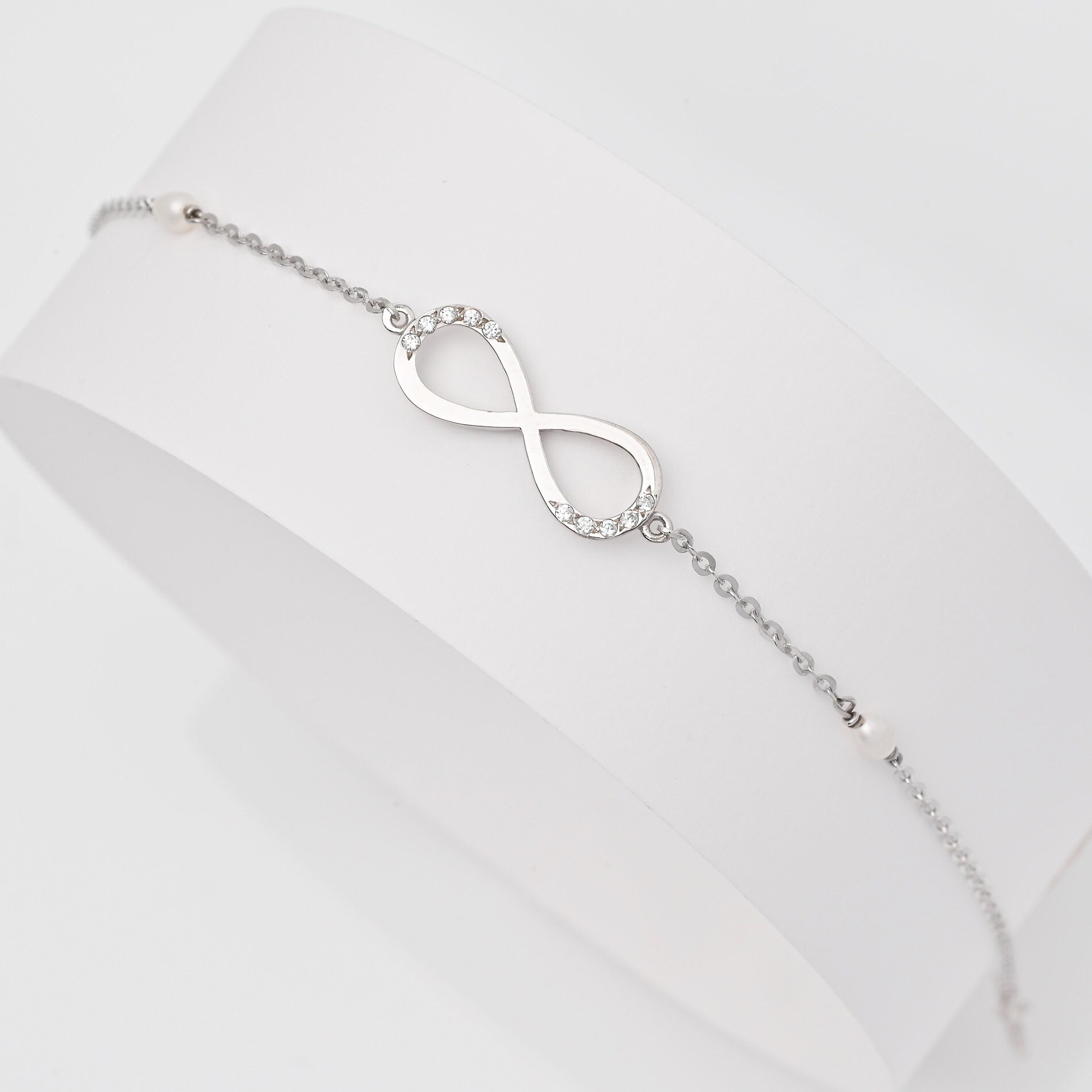 A women's bracelet featuring the infinity symbol in 14k white gold, adorned with cubic zirconia stones and pearls.