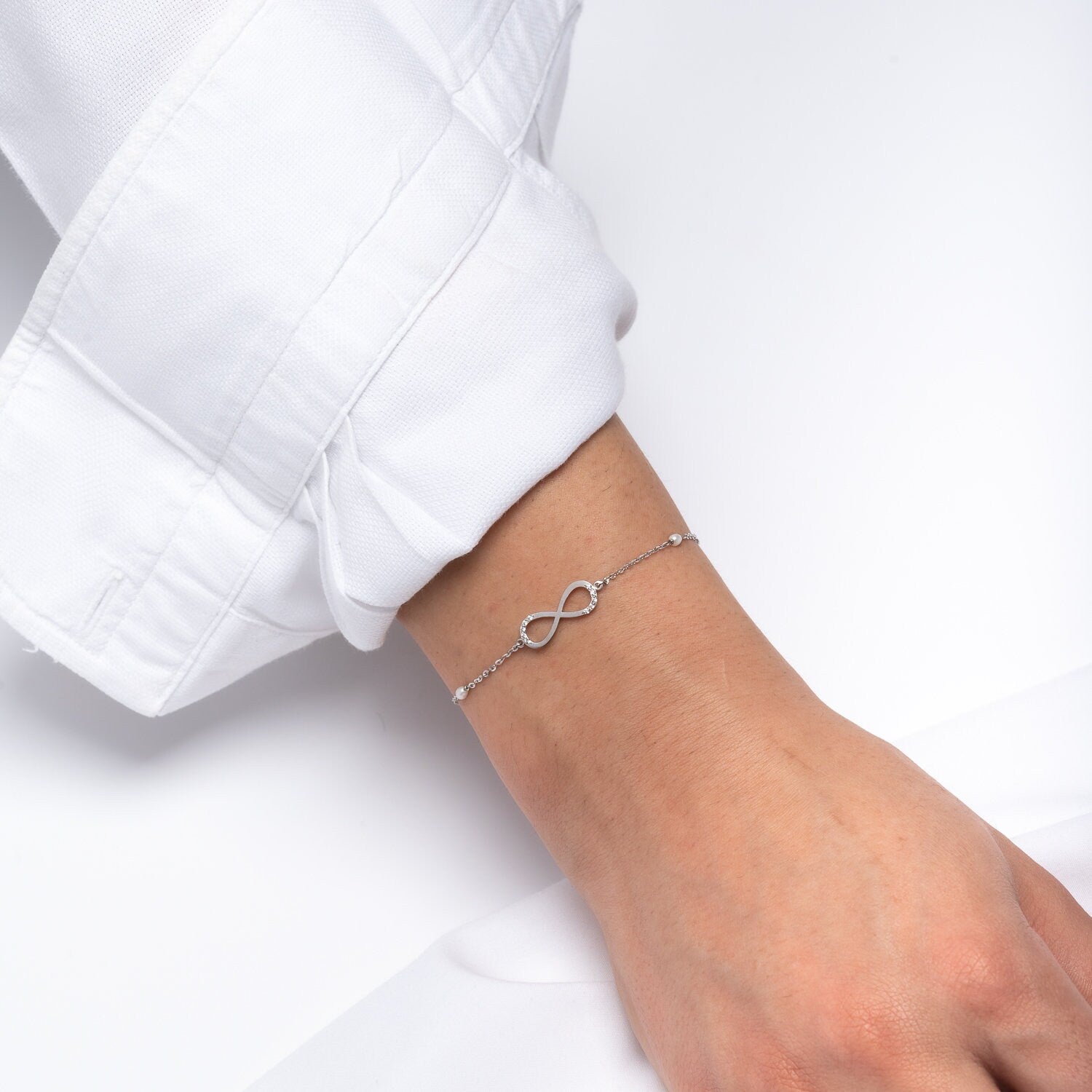 A women's bracelet featuring the infinity symbol in 14k white gold, adorned with cubic zirconia stones and pearls.