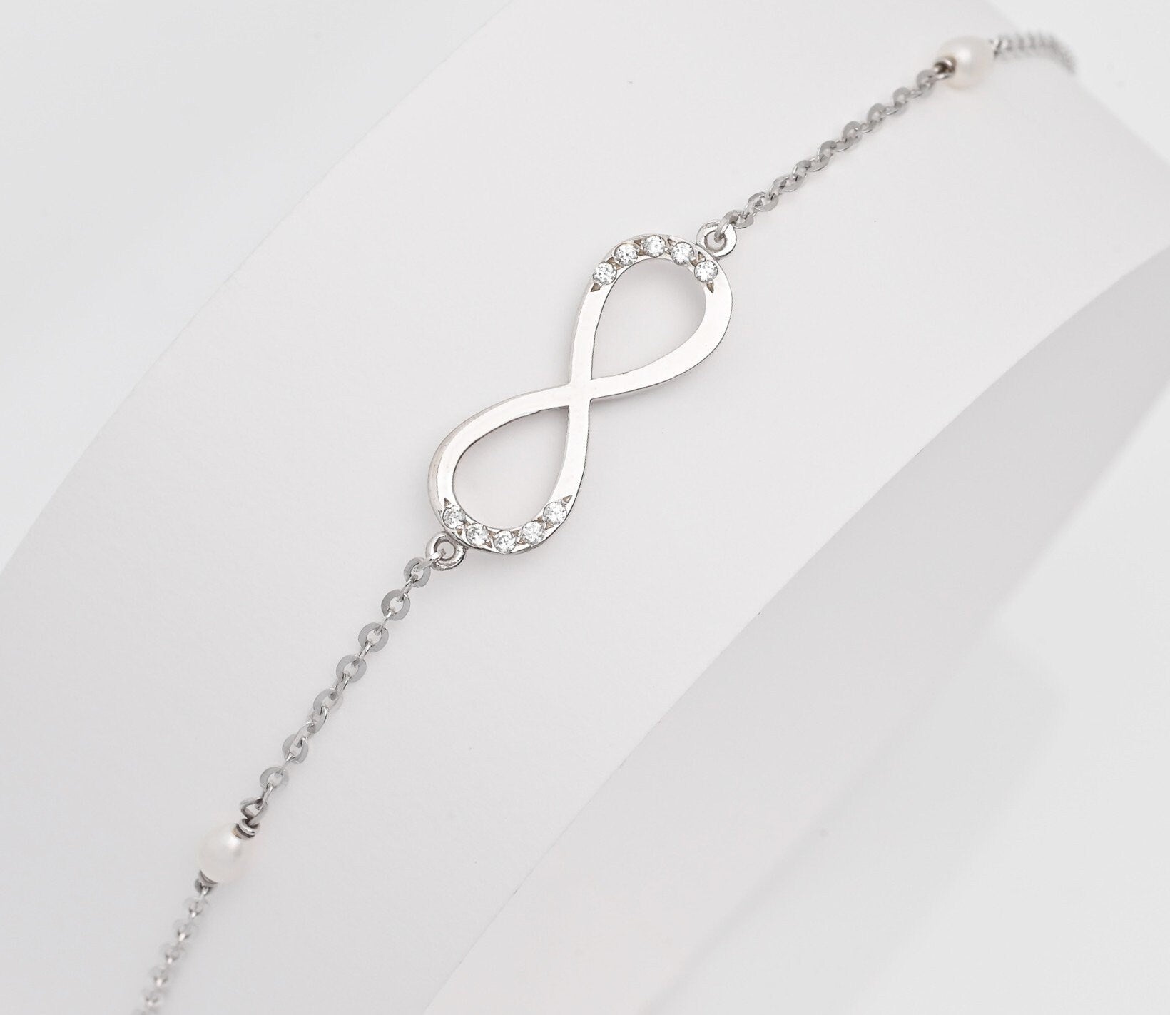 A women's bracelet featuring the infinity symbol in 14k white gold, adorned with cubic zirconia stones and pearls.