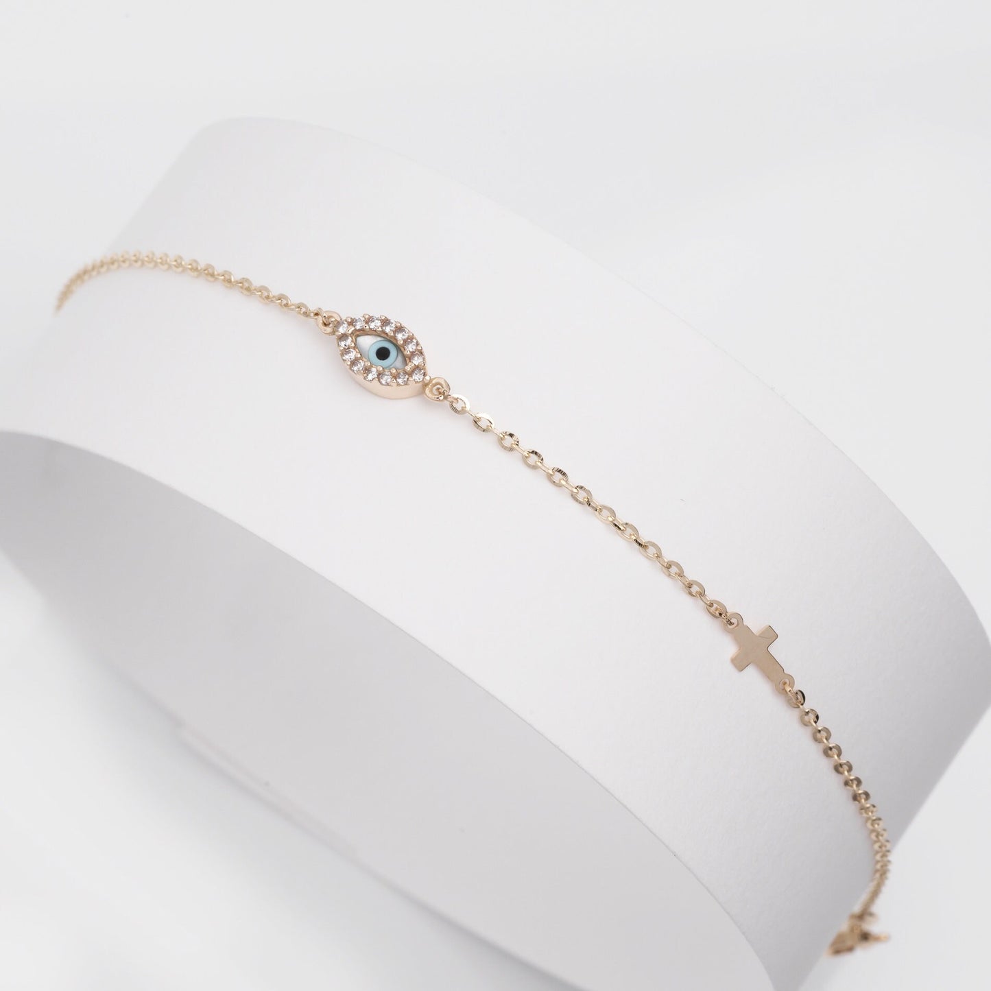 An oval evil eye bracelet adorned with cubic zirconia stones and a small cross.