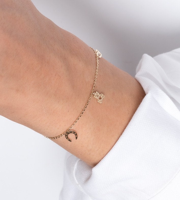 14k gold bracelet with hangginh charms, cross, heart, bear, horseshoe worn by a model 