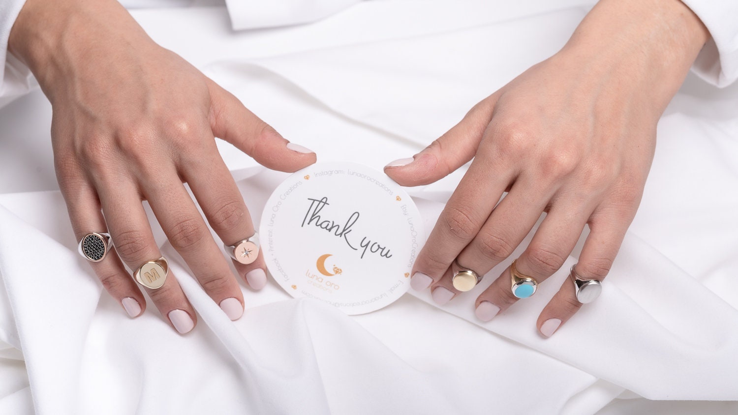 The image shows a close-up of a person's hands wearing several elegant rings in different styles, including a gold signet ring, a turquoise stone ring, and engraved rings