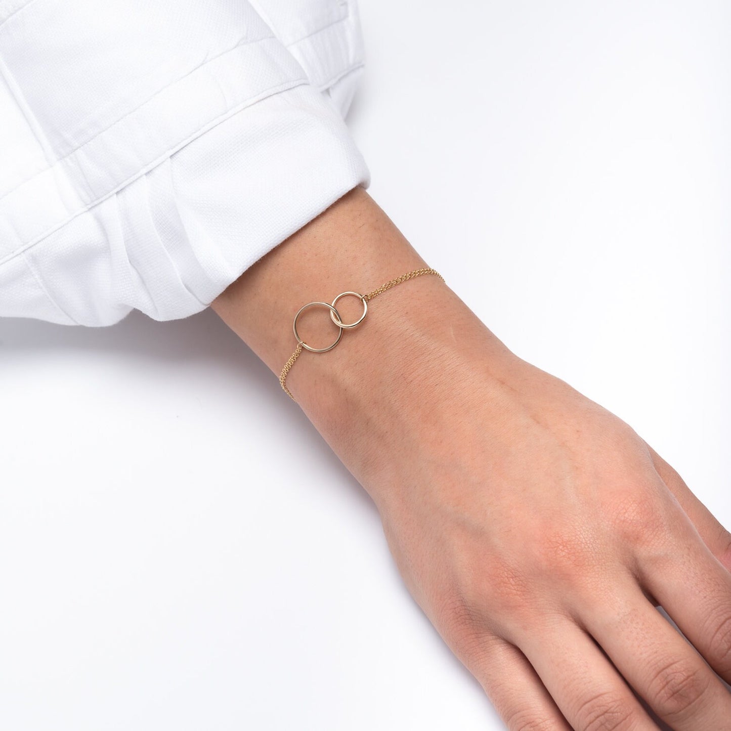 A model wears an interlocking bracelet crafted from 14k gold, featuring a double chain design.