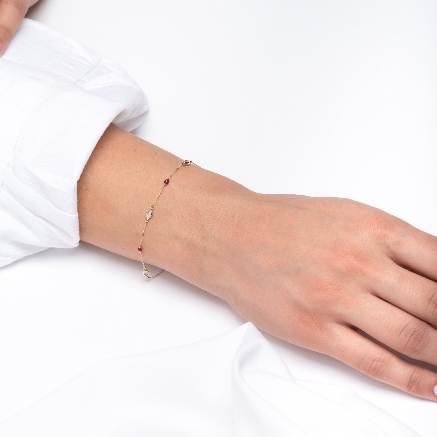 A 14k gold station bracelet adorned with mother of pearl and tourmaline worn by a model 