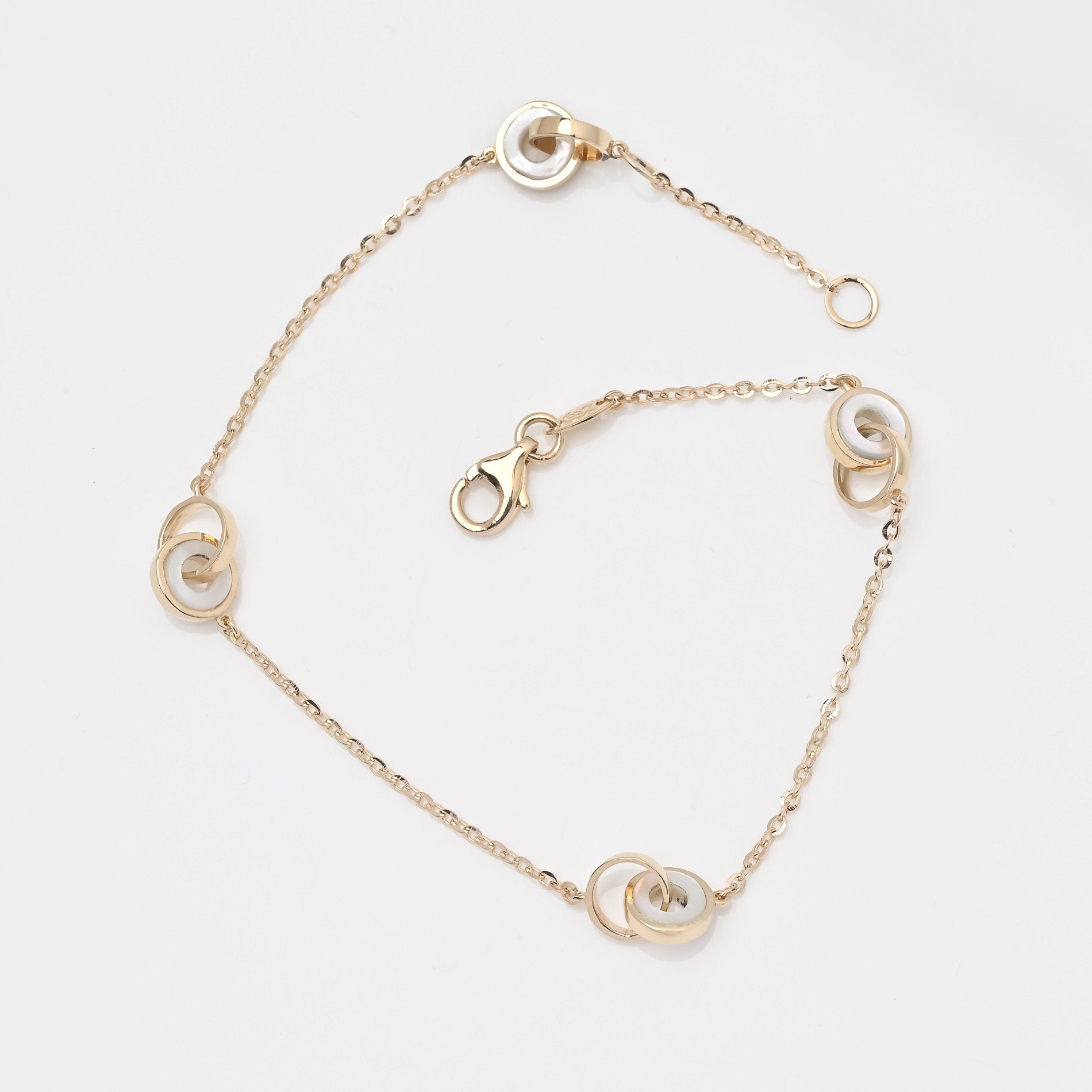 This image shows a delicate gold chain bracelet featuring three interlocking circle motifs. The circles appear to have a blend of gold and mother-of-pearl accents, giving the bracelet an elegant and minimalist look. 