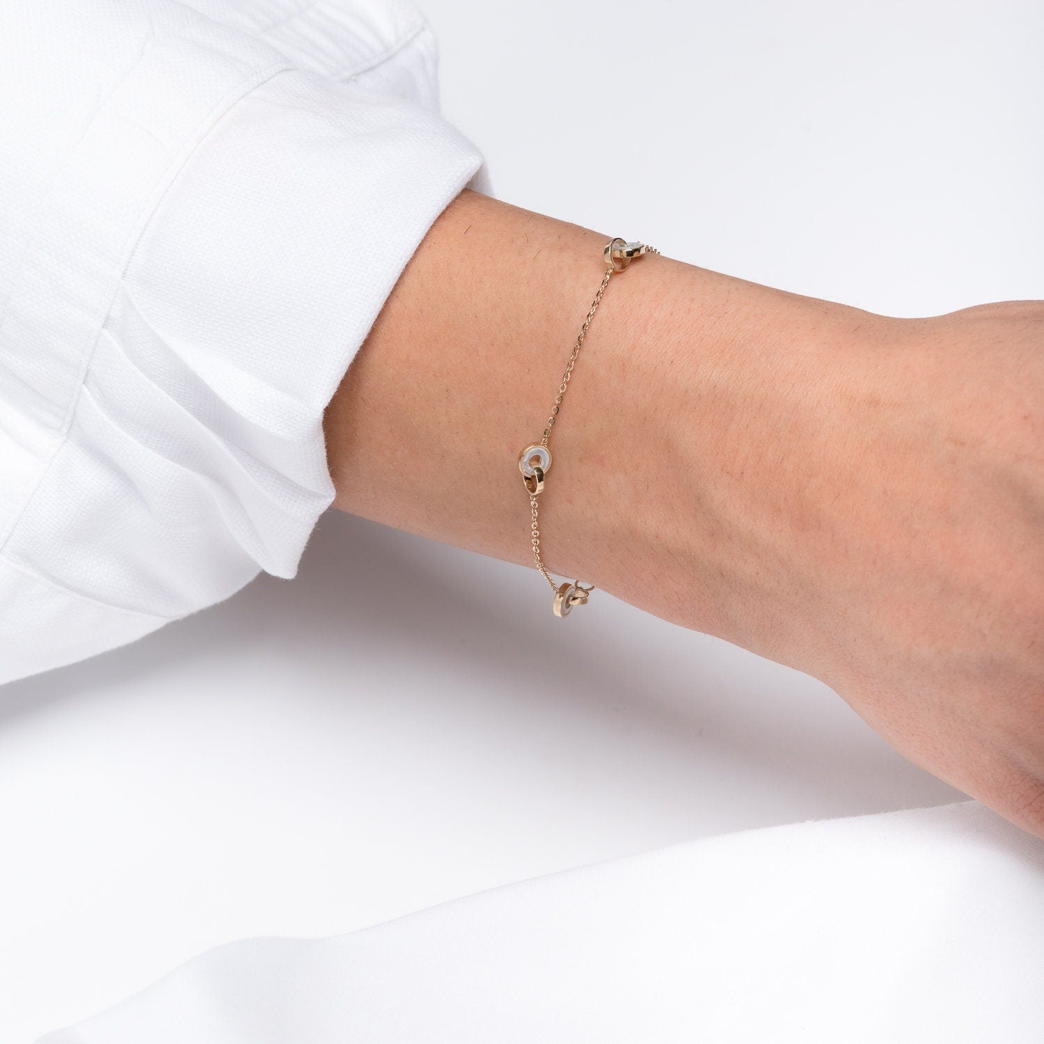 This image shows a delicate gold chain bracelet featuring three interlocking circle motifs. The circles appear to have a blend of gold and mother-of-pearl accents, giving the bracelet an elegant and minimalist look. 