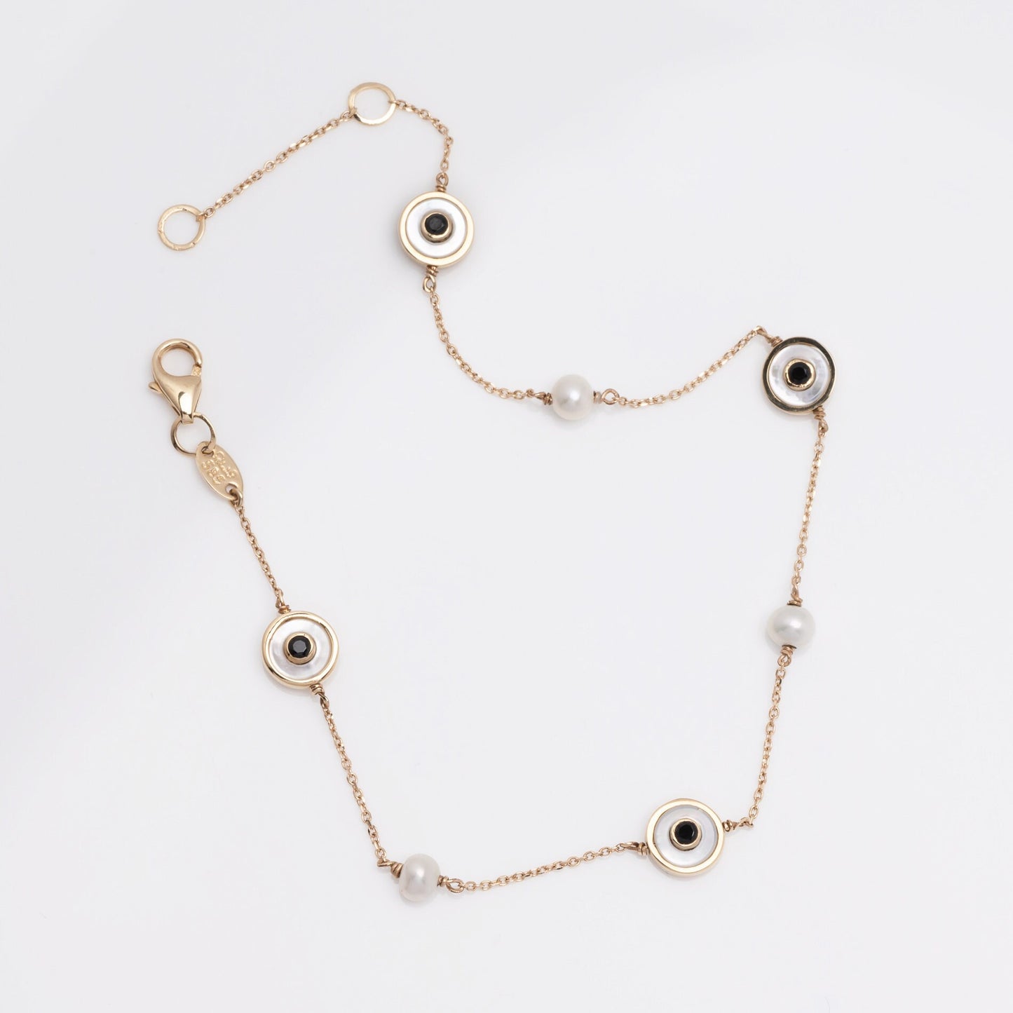 The photo shows a delicate 14k gold station bracelet with circular accents. Each station features alternating black and clear gemstones, set within gold bezels, and interspersed with small pearls along a fine chain.