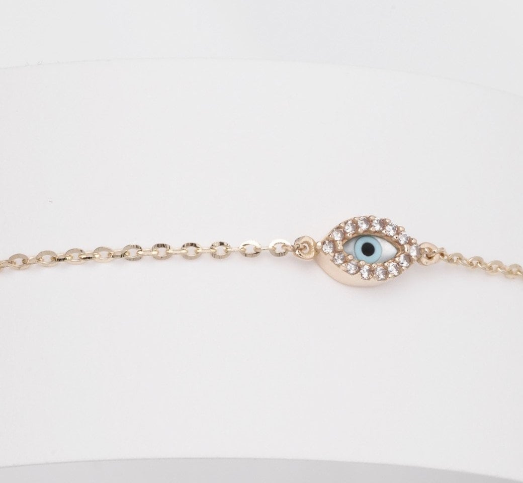 An oval evil eye bracelet adorned with cubic zirconia stones and a small cross.