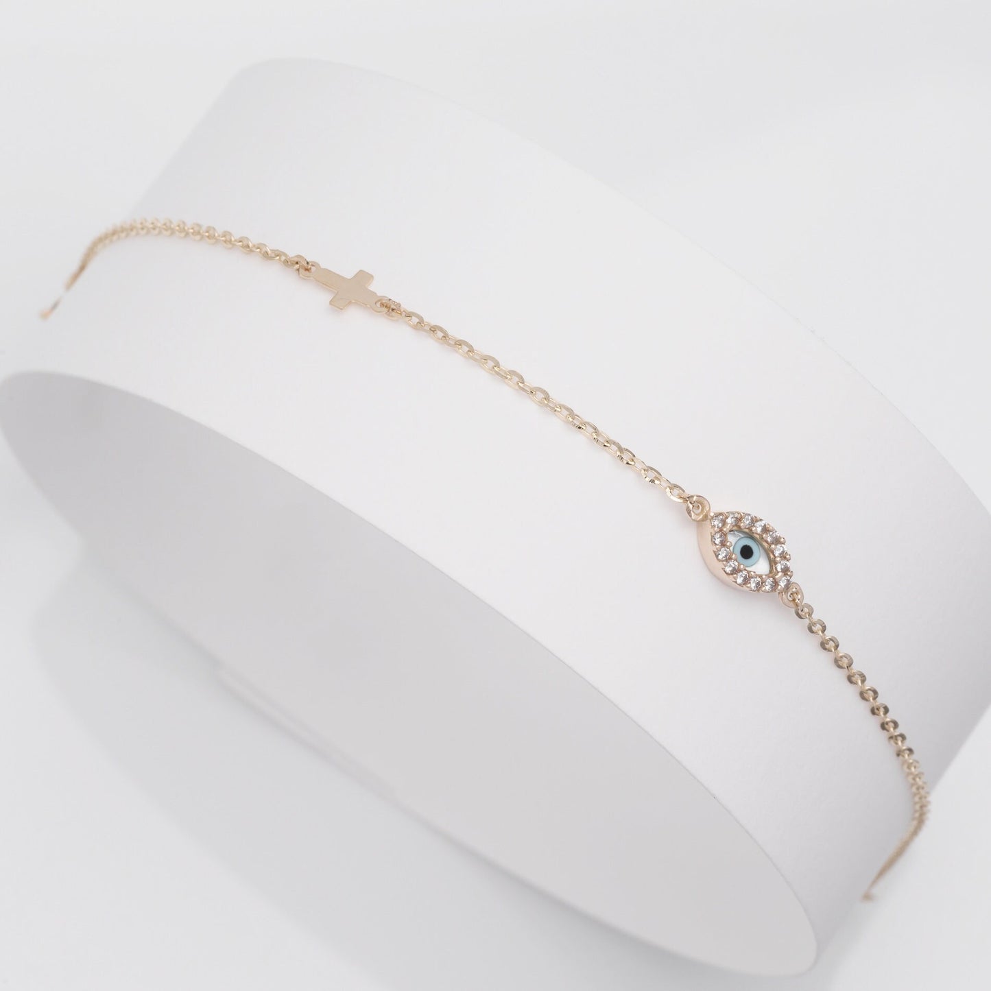 An oval evil eye bracelet adorned with cubic zirconia stones and a small cross.