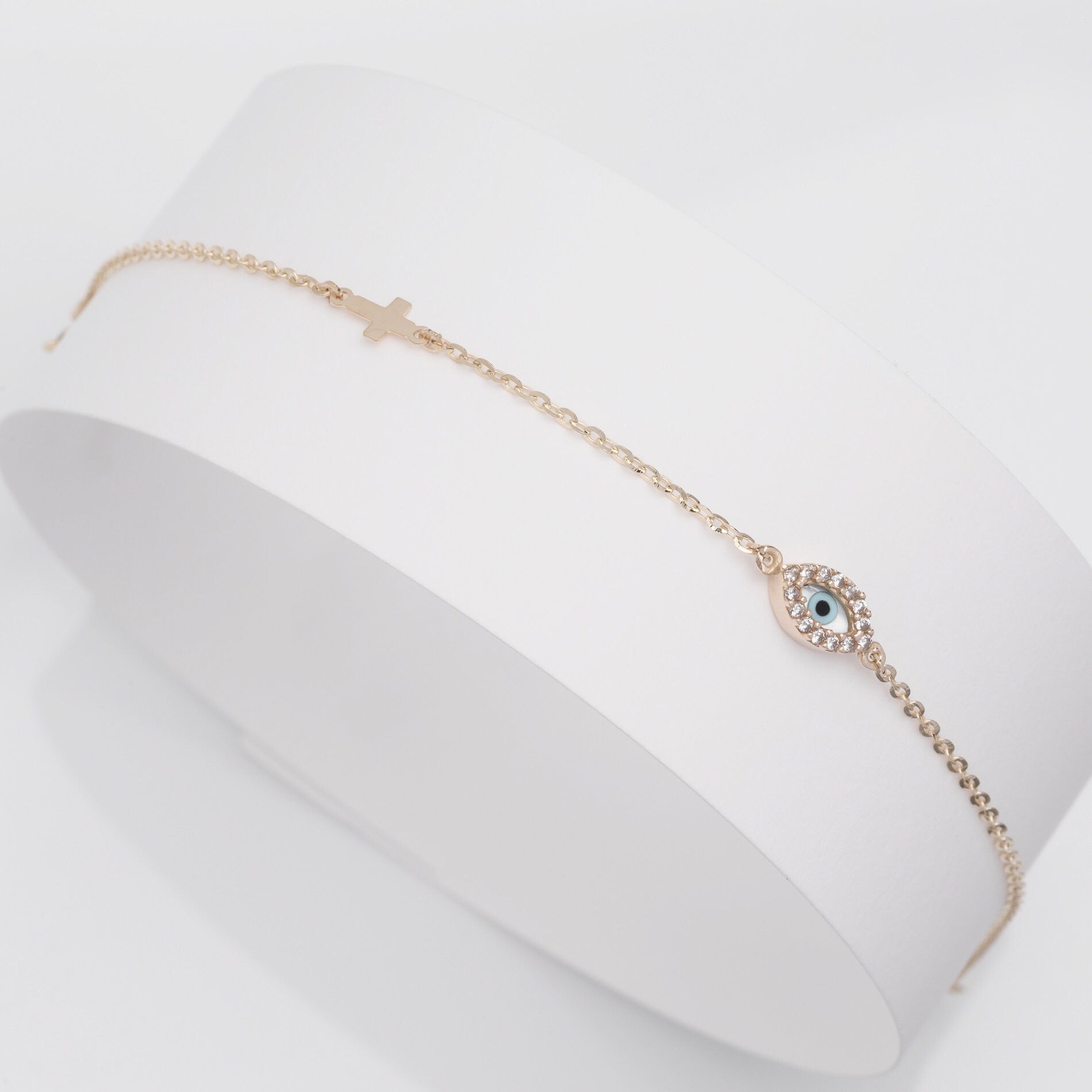 An oval evil eye bracelet adorned with cubic zirconia stones and a small cross.