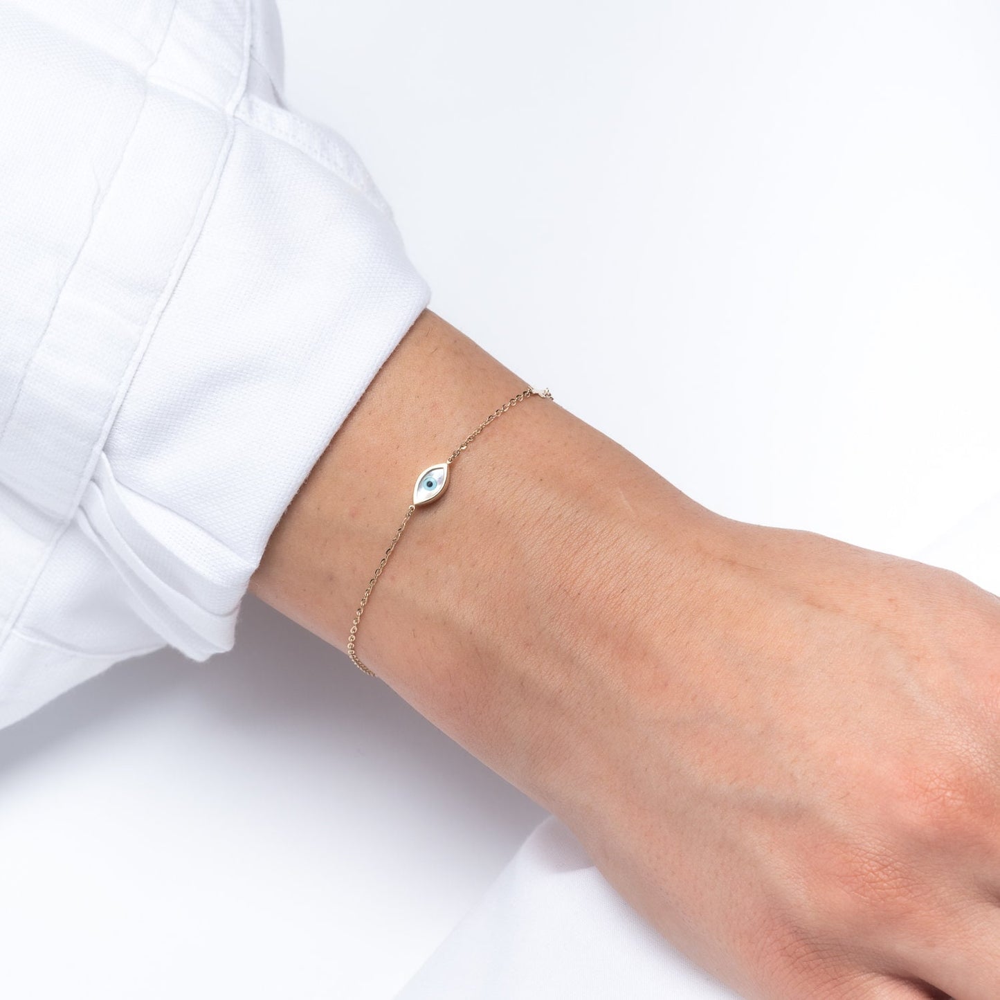 An oval evil eye bracelet adorned with cubic zirconia stones and a small cross worn by a model 