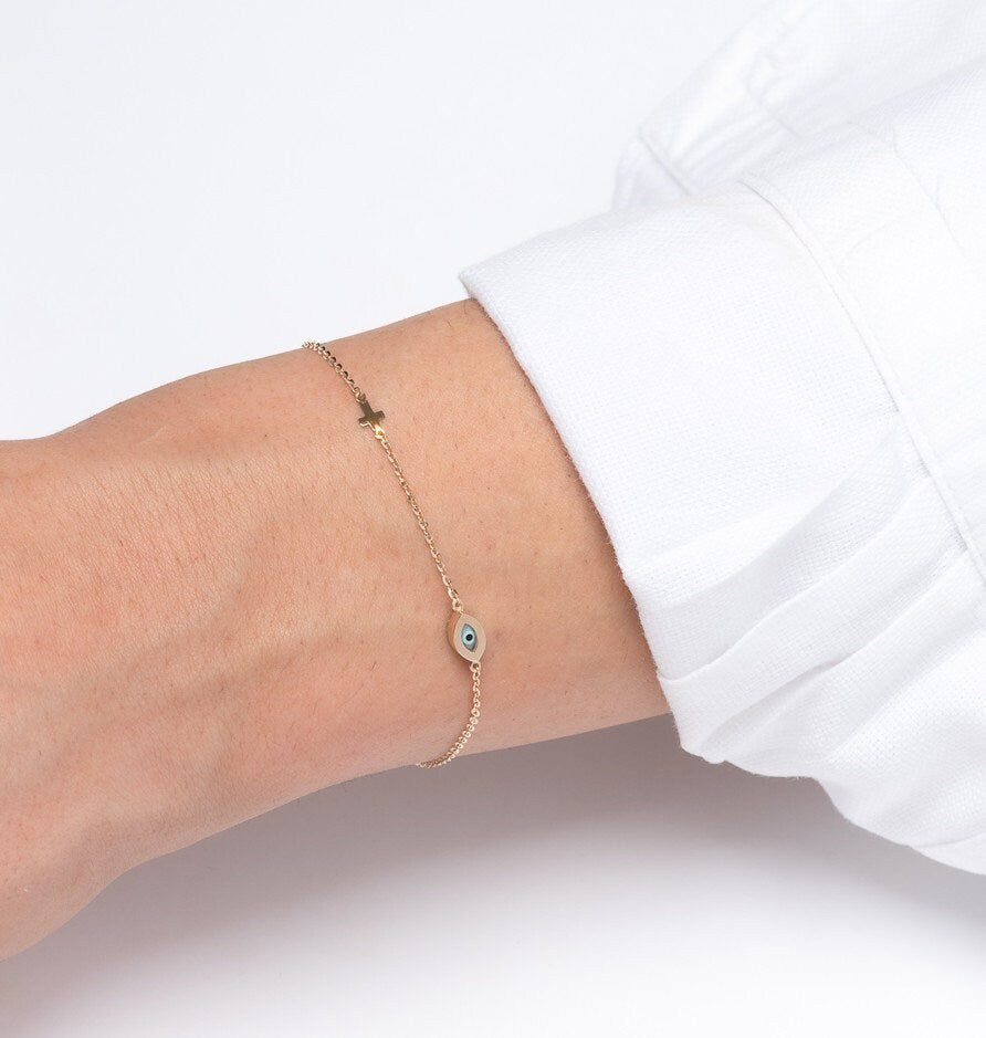 An oval evil eye bracelet adorned with cubic zirconia stones and a small cross worn by a model 