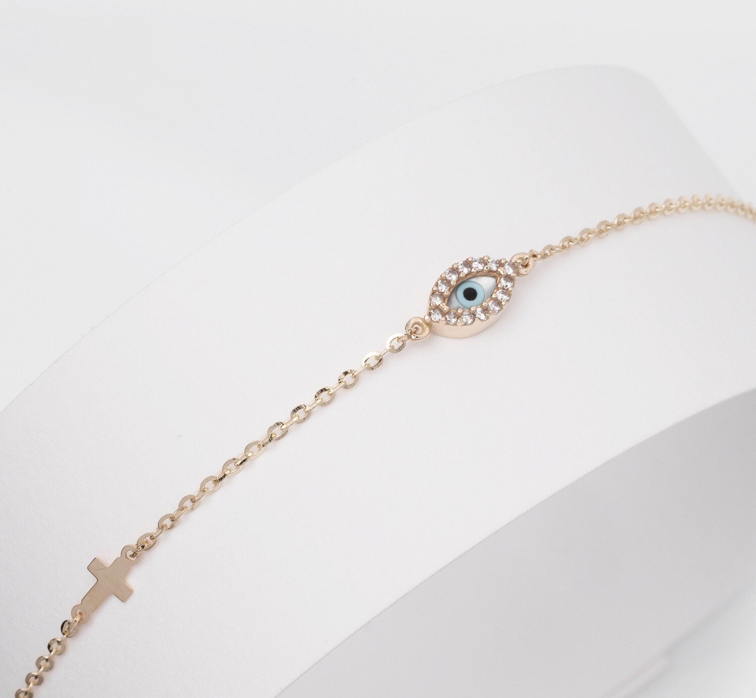 An oval evil eye bracelet adorned with cubic zirconia stones and a small cross.