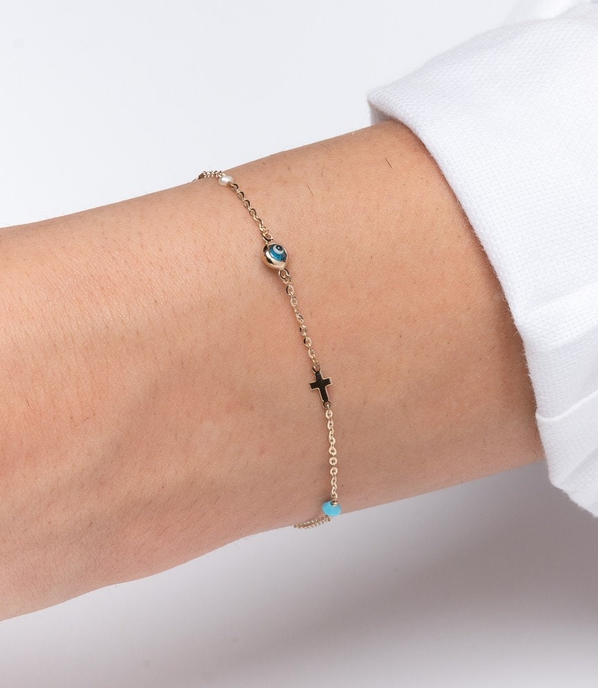 evil eye bracelet with cross, heart, pearl, turqoise stone in 14k solid gold worn by a model 