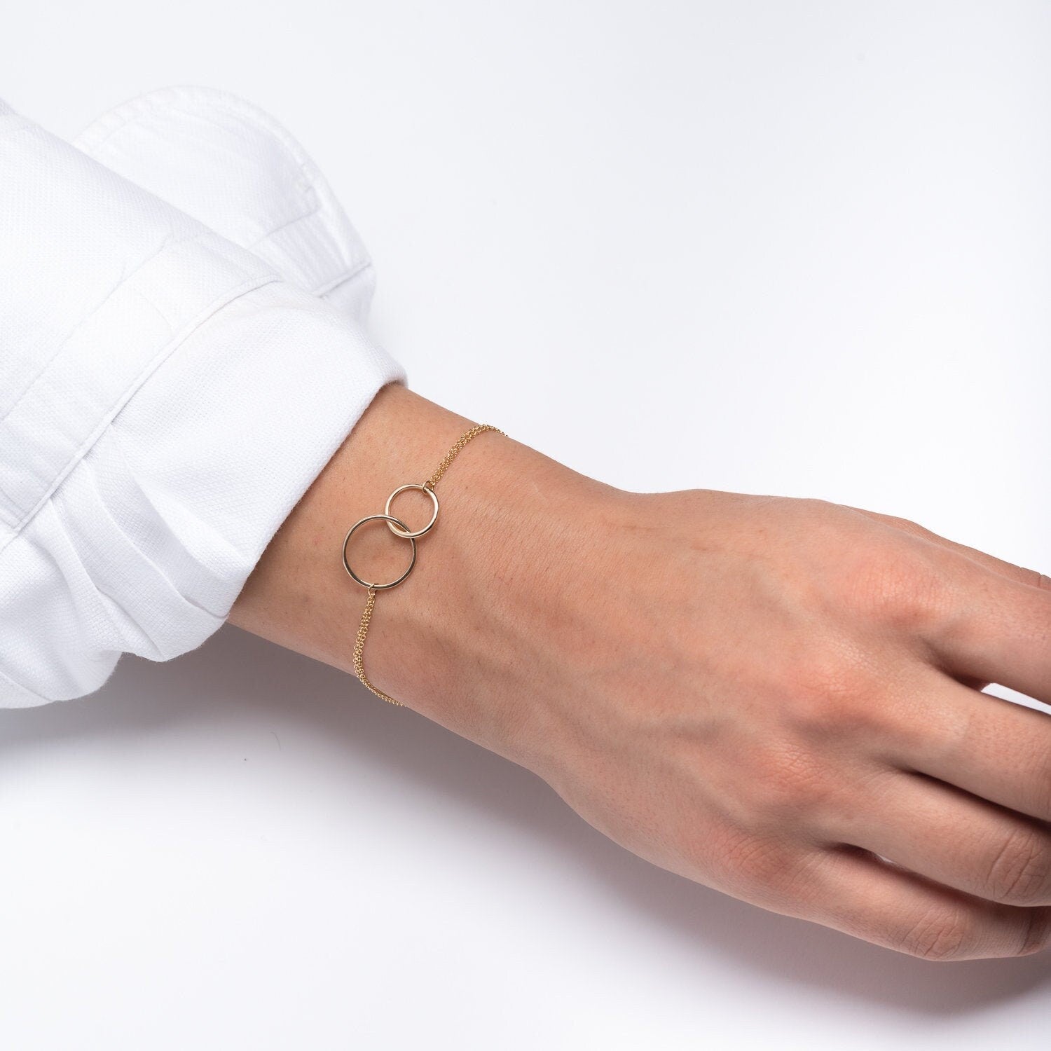 A model wears an interlocking bracelet crafted from 14k gold, featuring a double chain design.