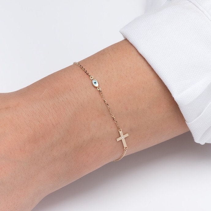 diamond cross and evil eye bracelet in 14k yellow gold worn by a model 