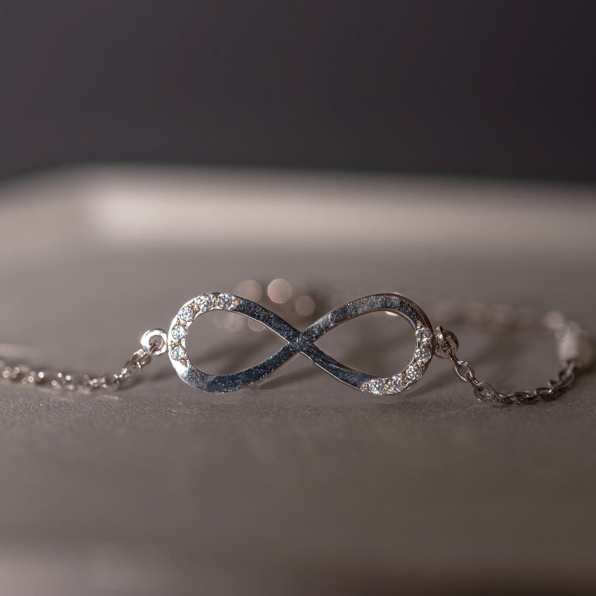 A women's bracelet featuring the infinity symbol in 14k white gold, adorned with cubic zirconia stones and pearls.