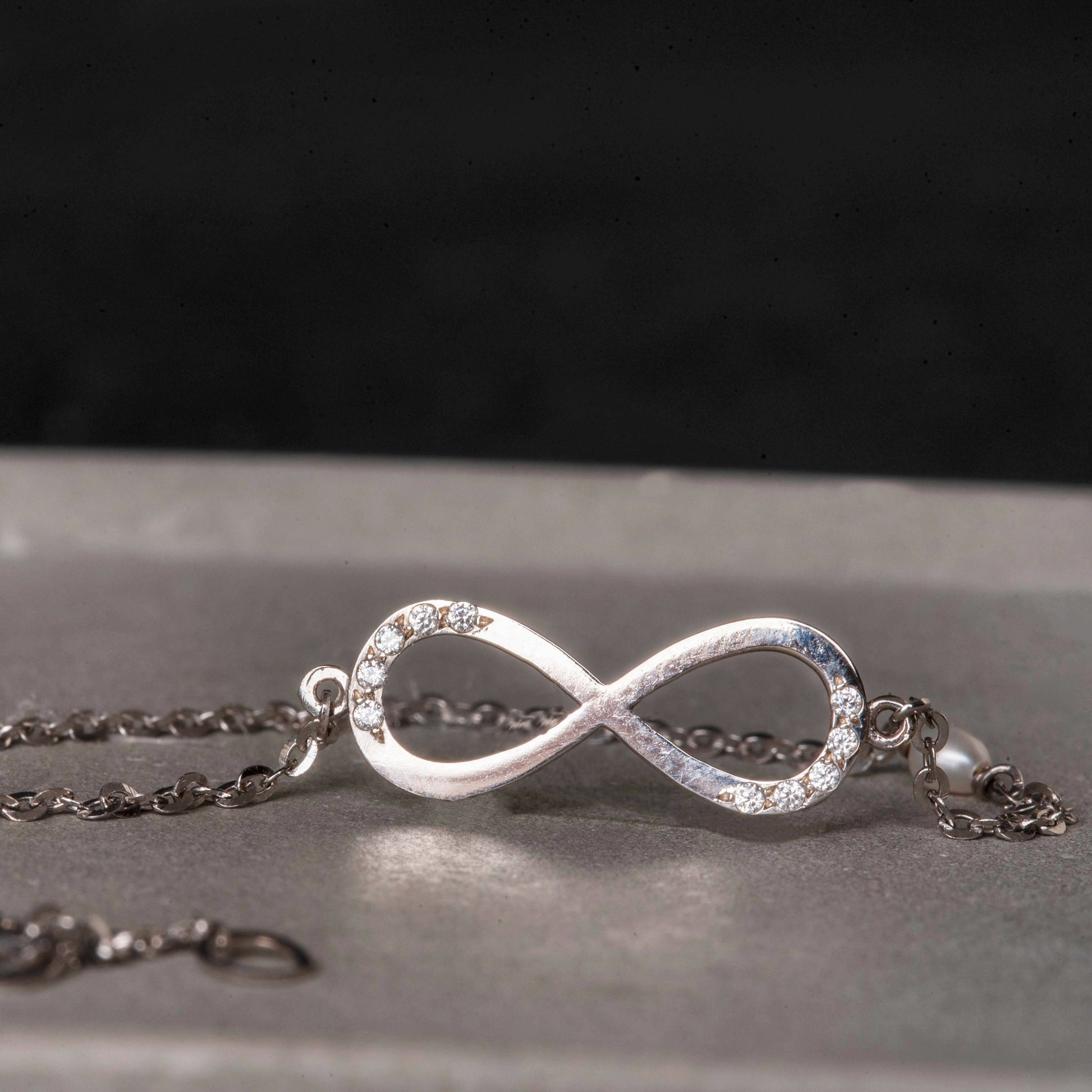 A women's bracelet featuring the infinity symbol in 14k white gold, adorned with cubic zirconia stones and pearls.