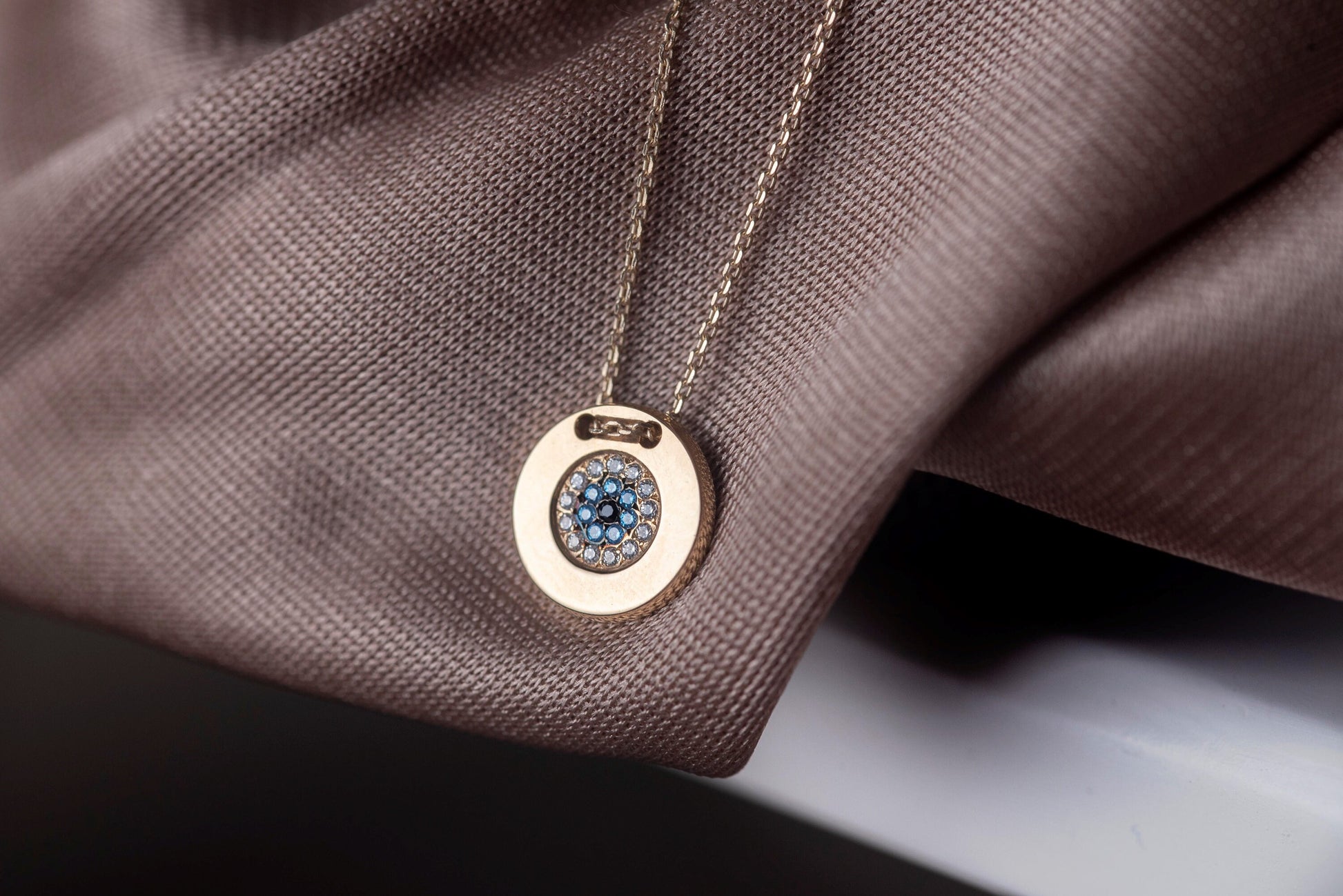 A women's round evil eye necklace, encrusted with cubic zirconia stones and crafted in 14k gold.