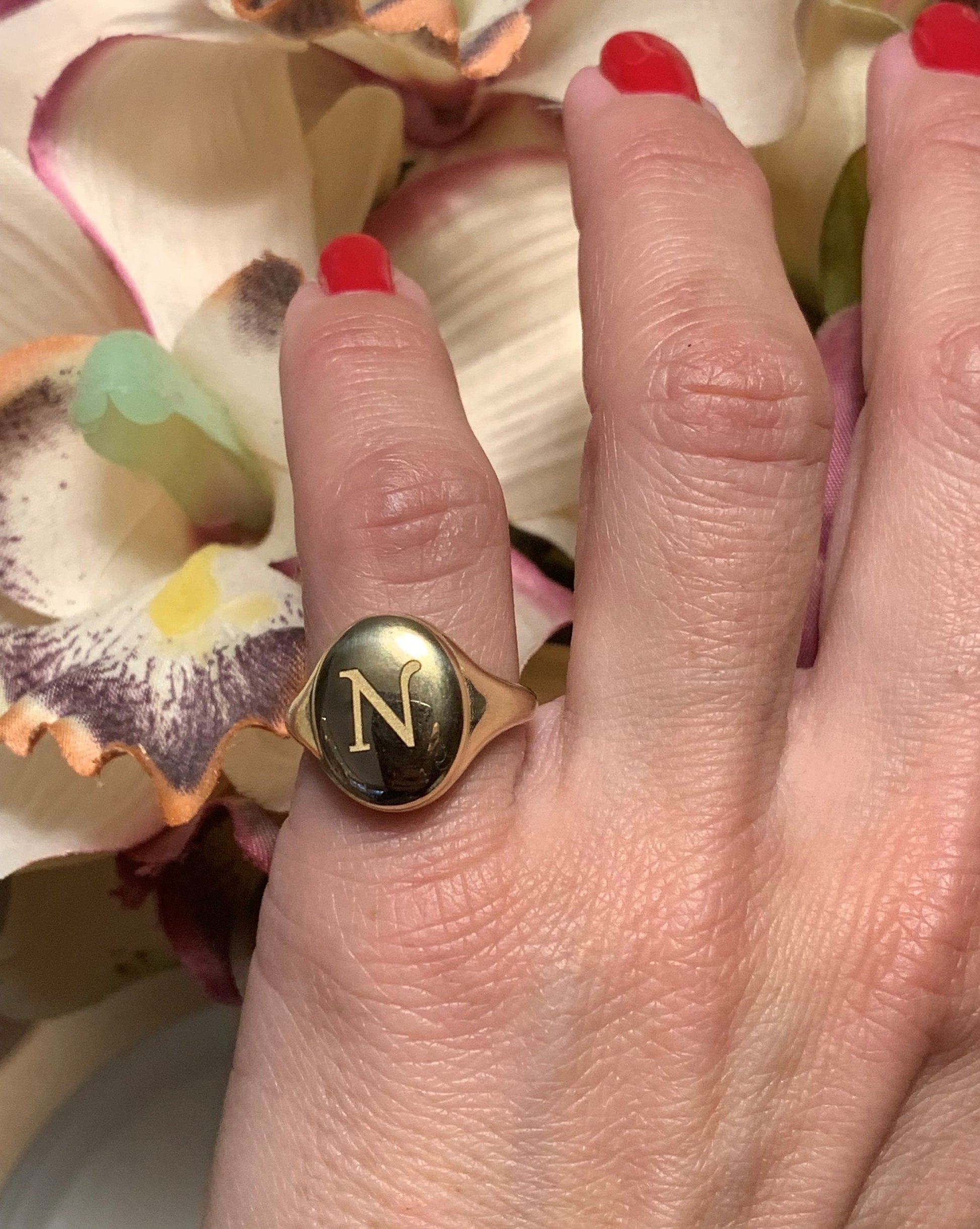 An oval signet ring in 14k gold, showcased by a model and engraved with an initial.