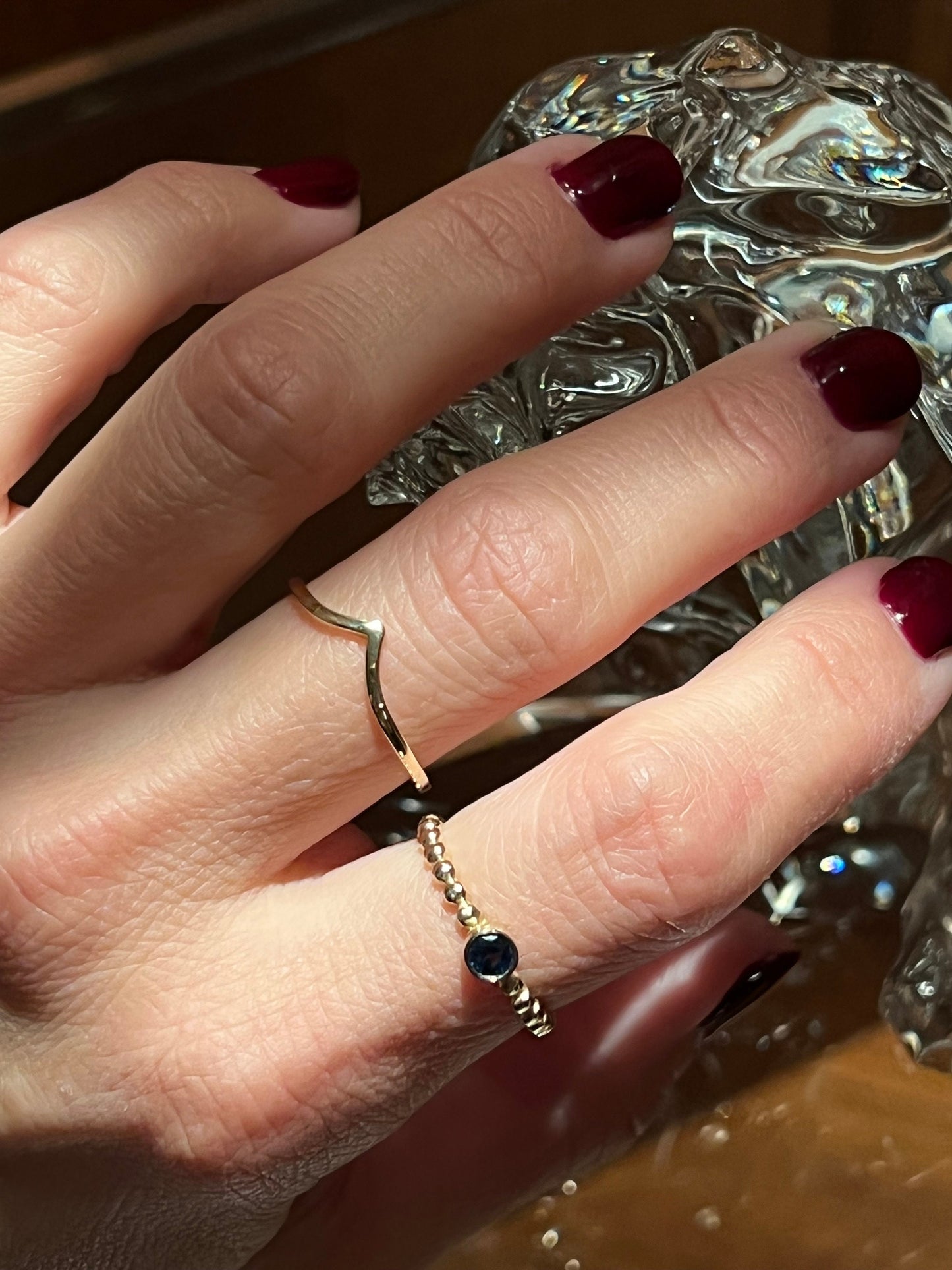 A sapphire birthstone beaded ring in 14k gold alongside a slender chevron 14k gold ring, both adorned on a hand.