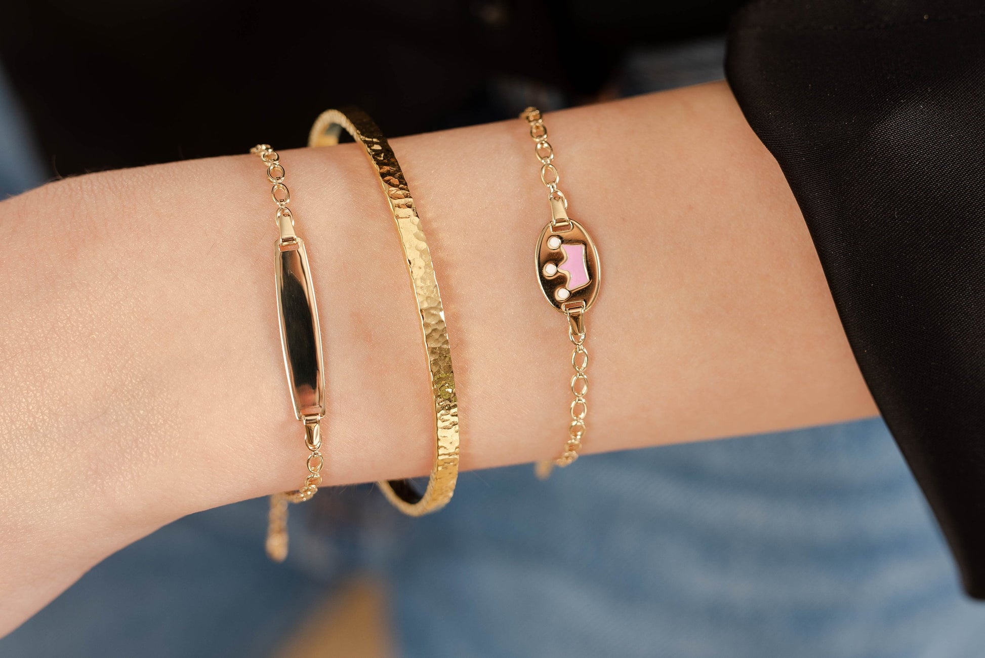 a hand wearing a hammered bangle bracelet, one id bracelet and one crown enamel bracelet