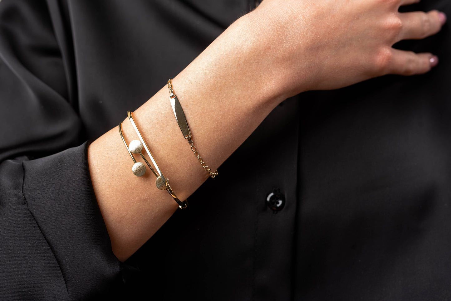 This is an image featuring several gold bracelets on a person's wrist. The bracelets vary in style, including a delicate chain bracelet, a flat bar bracelet, and a couple of minimalist bangle designs.t ID solid 14k gold bracelet