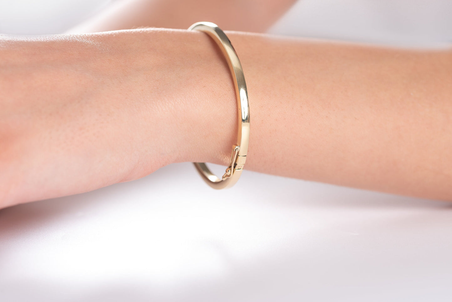 A 3.40mm hinged bangle bracelet in 14k gold, showcased by a model, is an elegant choice for women.