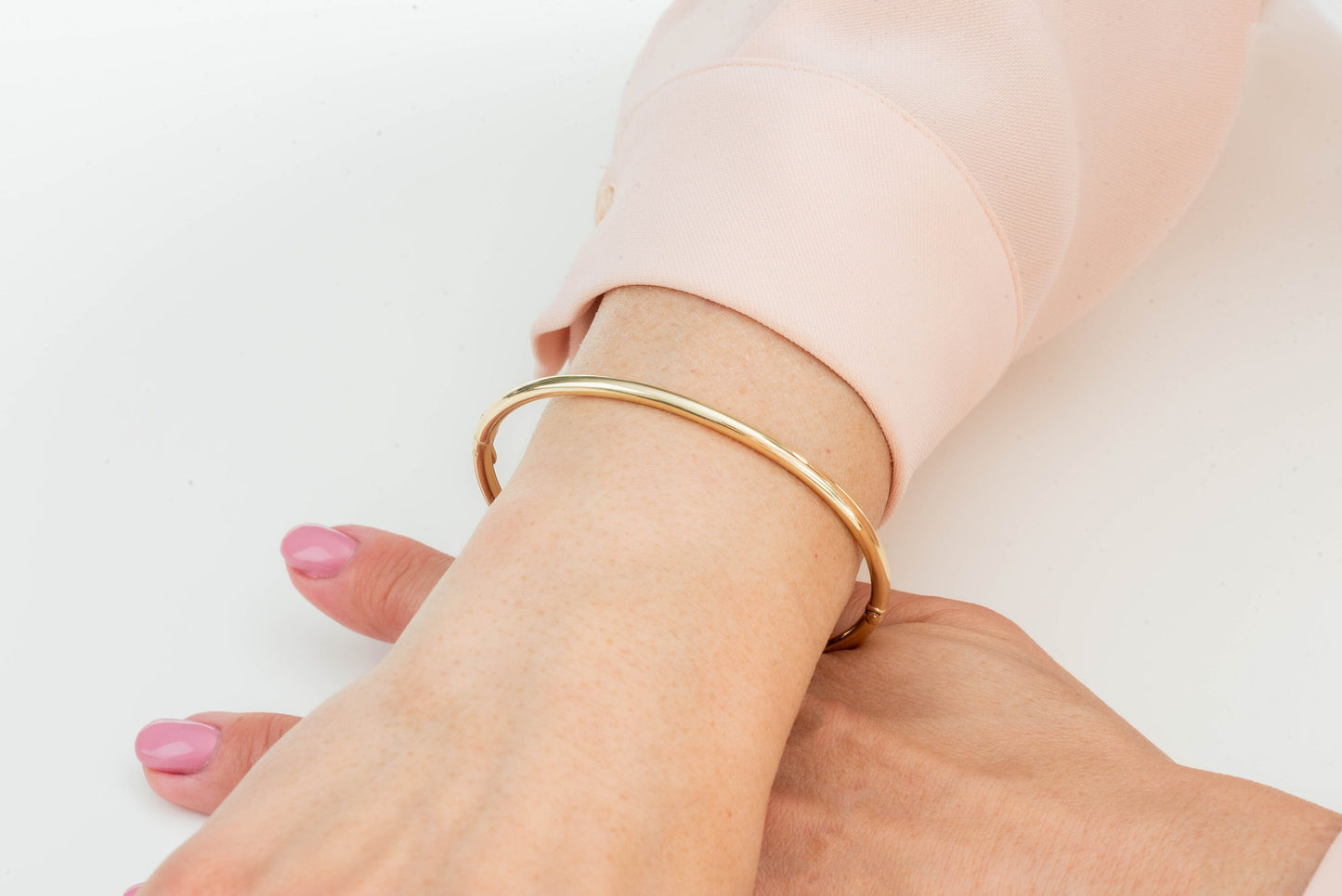 A round bangle bracelet made of 14k gold, displayed on a wrist.